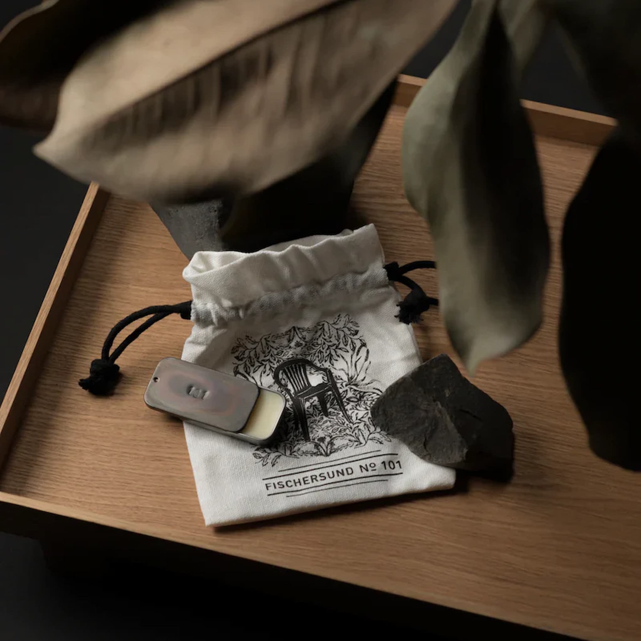 Tin of Fischersund solid perfume on a drawstring bag on a wooden surface, with leaves nearby