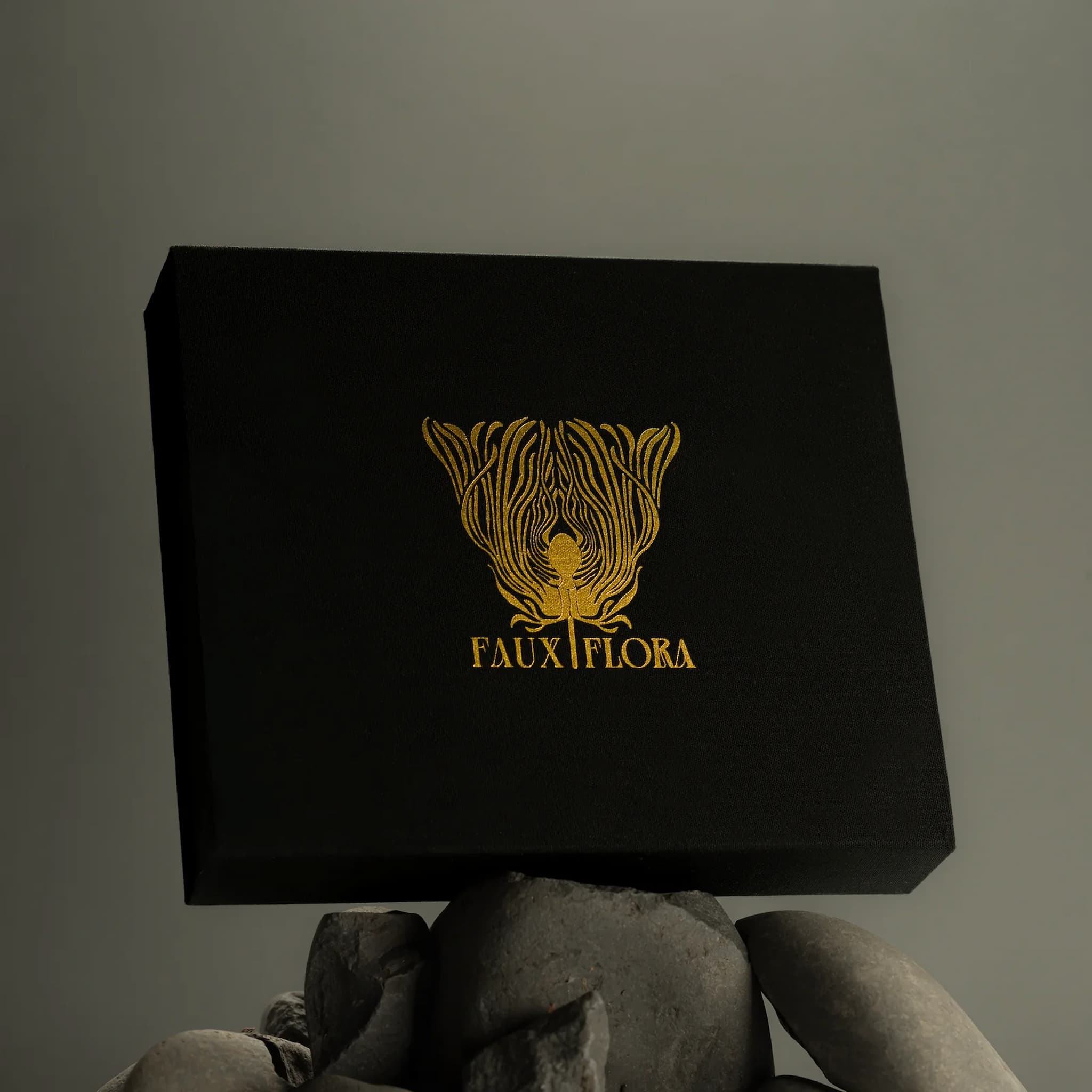 Black Fischersund discovery set box with gold 'FAUX FLORA' logo on gray rocks against a gray background