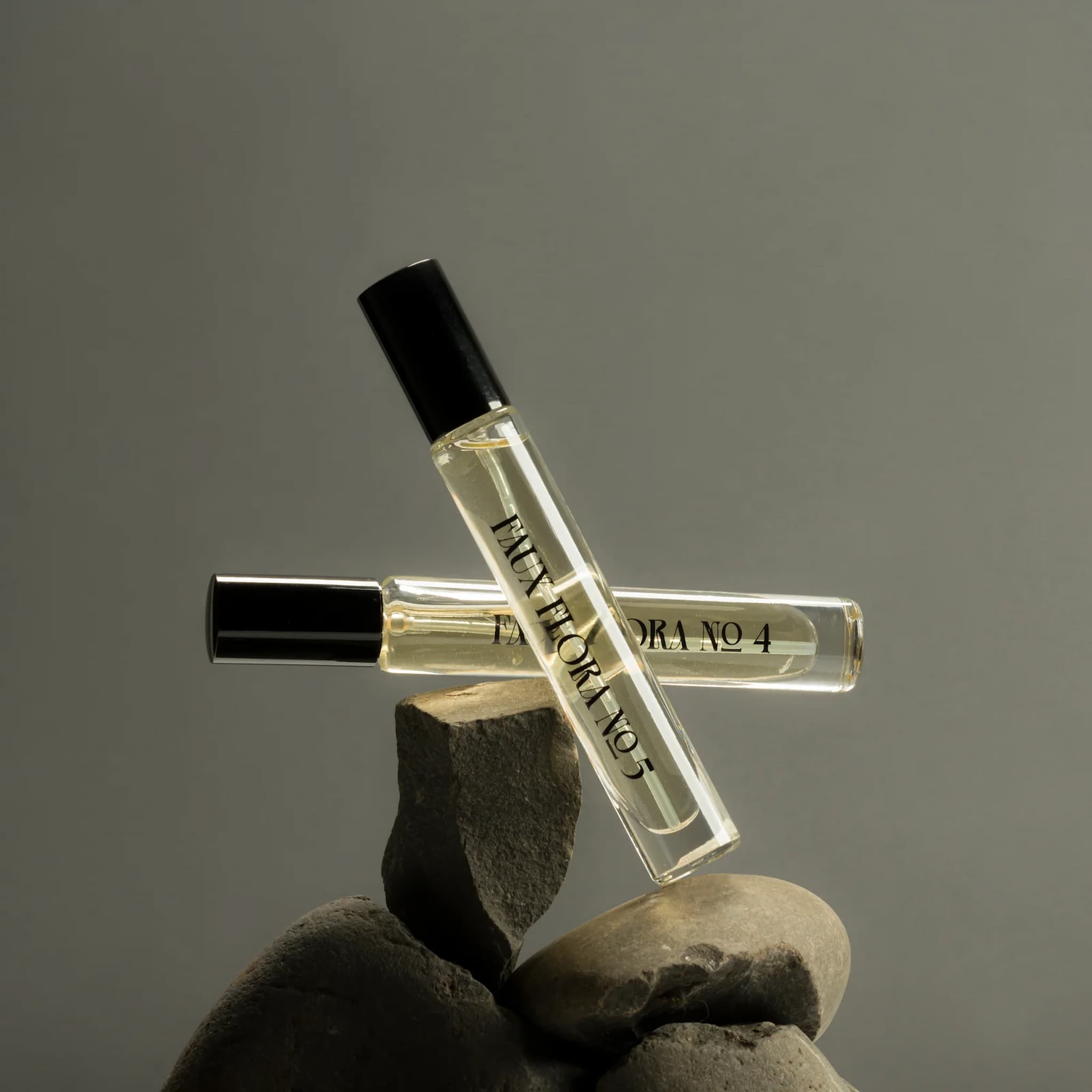 Two Fischersund Faux Flora perfume bottles with black caps on rocks against a gray background