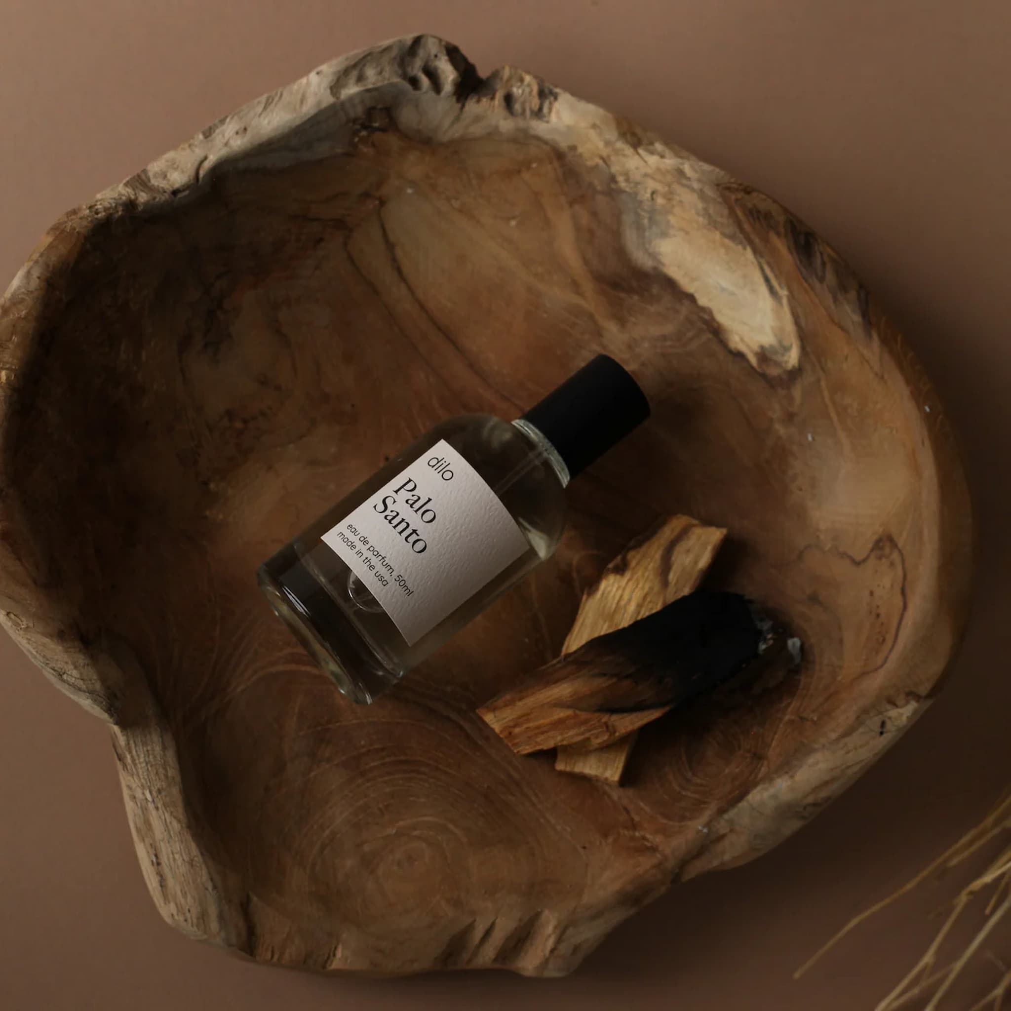Bottle of Dilo Palo Santo perfume in a wooden bowl on a brown background