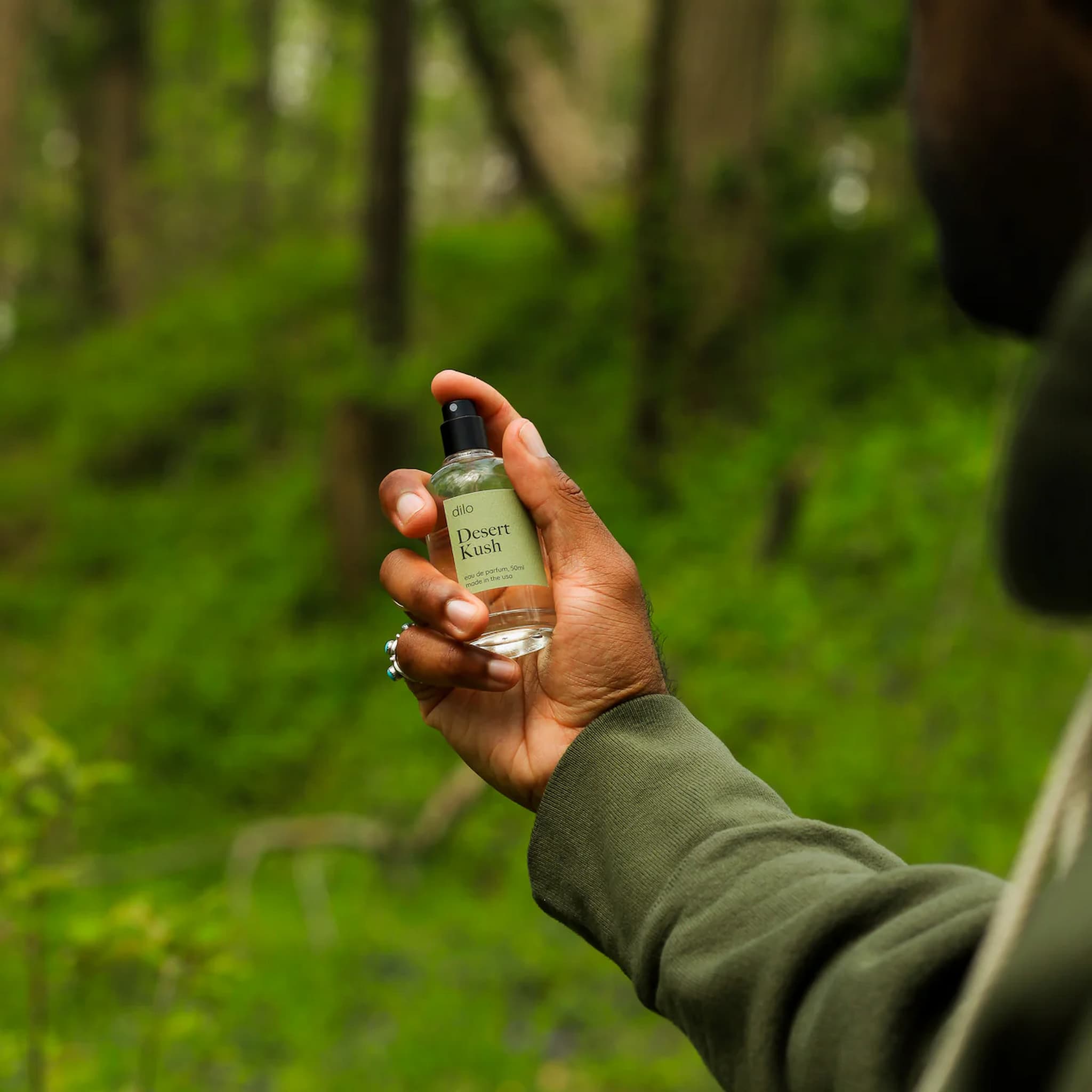 Hand holding a bottle of dilo Desert Kush perfume in a forest setting