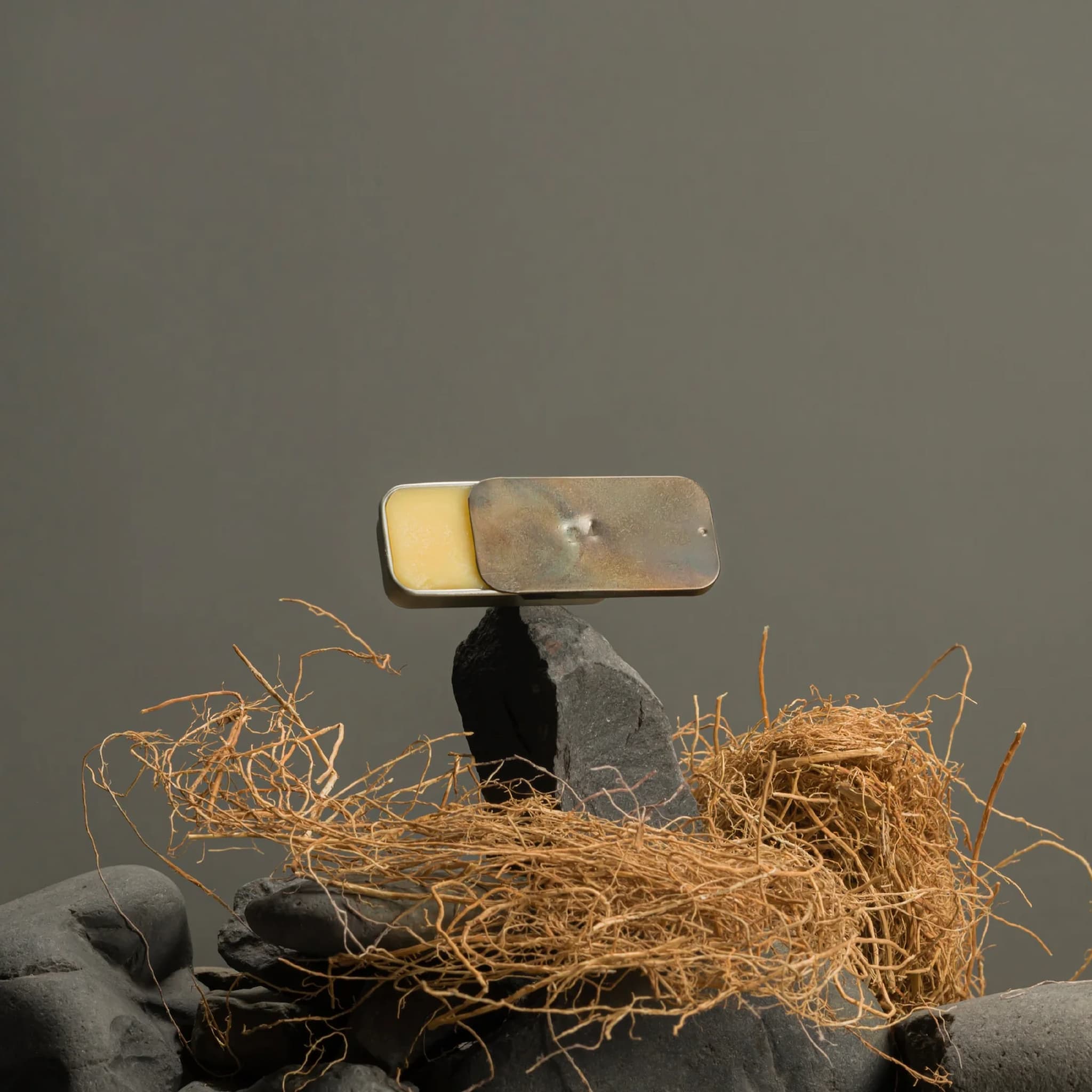 Metal tin of Fischersund solid perfume on a rock, surrounded by twigs against a dark background