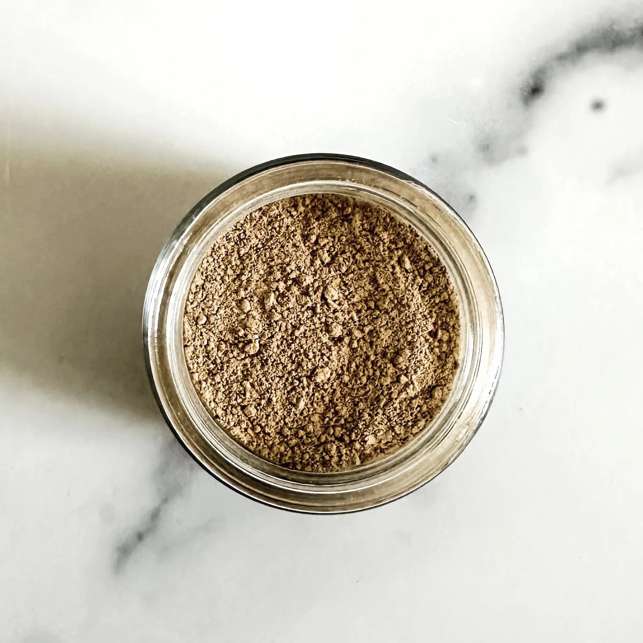 Glass jar filled with brown powder on a marble surface