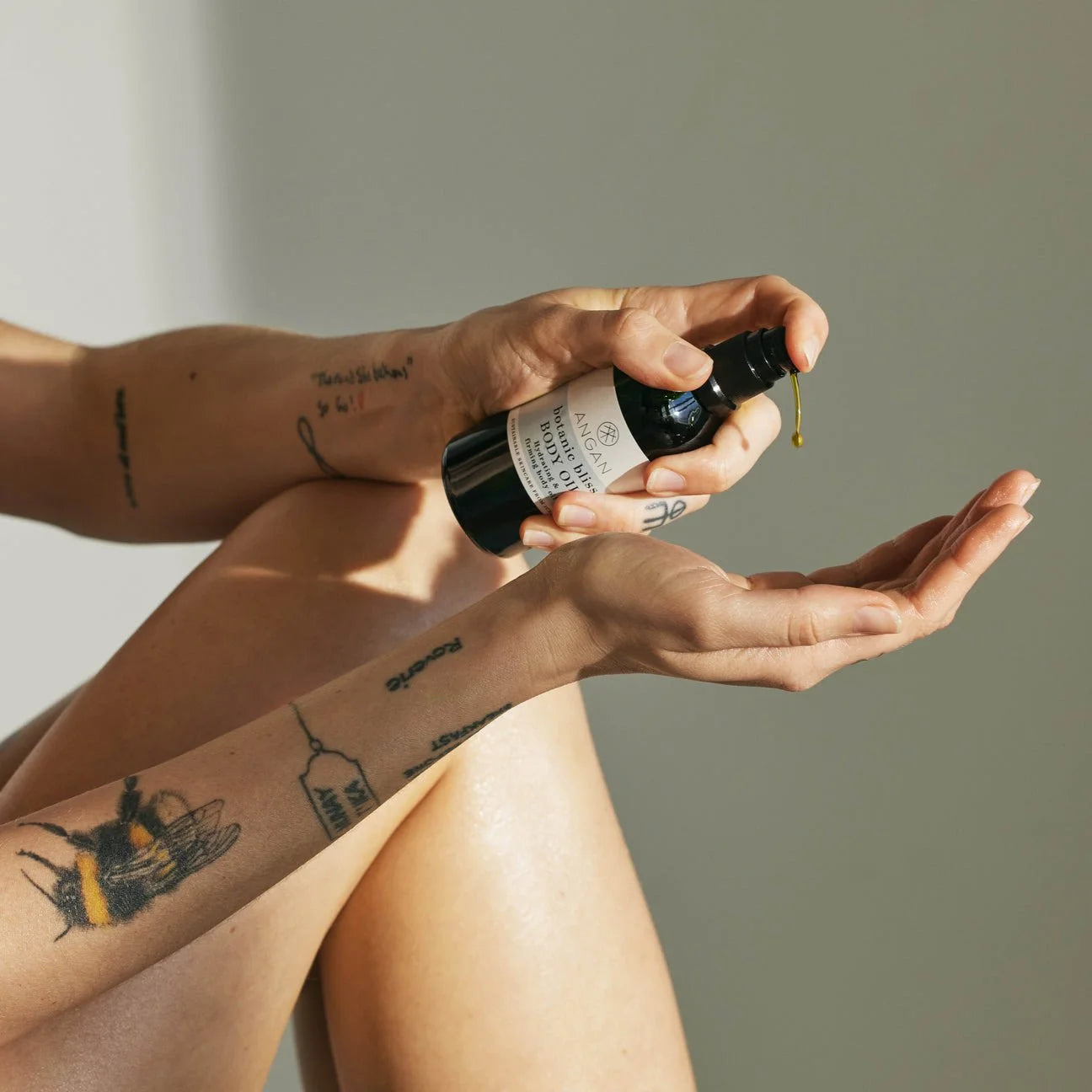 Person holding a bottle of Angan body oil with dropper over their palm against a neutral background