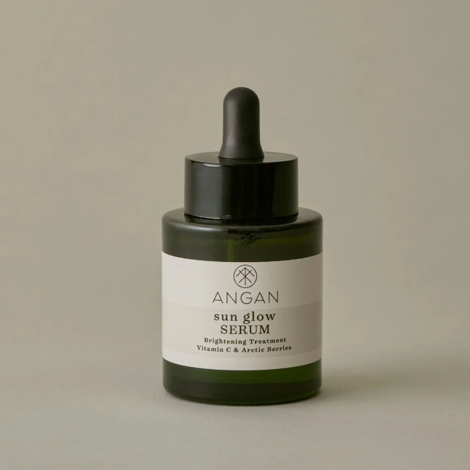Angan Sun Glow Serum in a dark green glass dropper bottle with a black dropper cap and a white label, set against a neutral beige background.