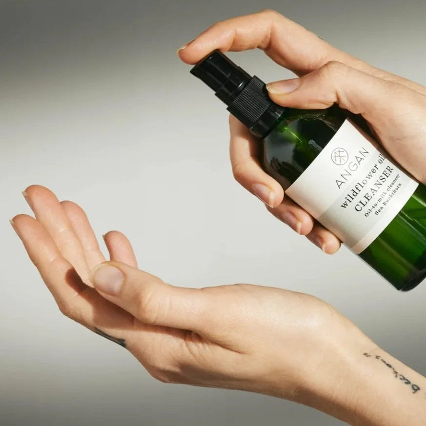 Person holding a green bottle labeled 'ANGAN' with a white label over a neutral background