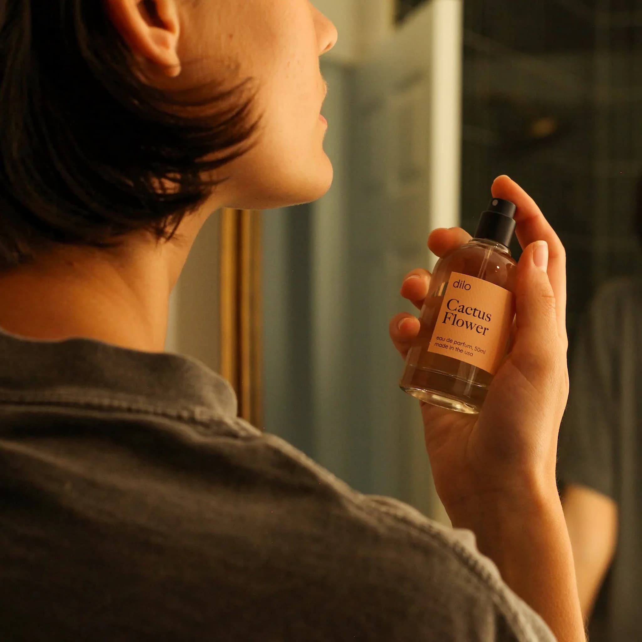Person holding a dilo perfume bottle labeled 'Cactus Flower' in front of a mirror.