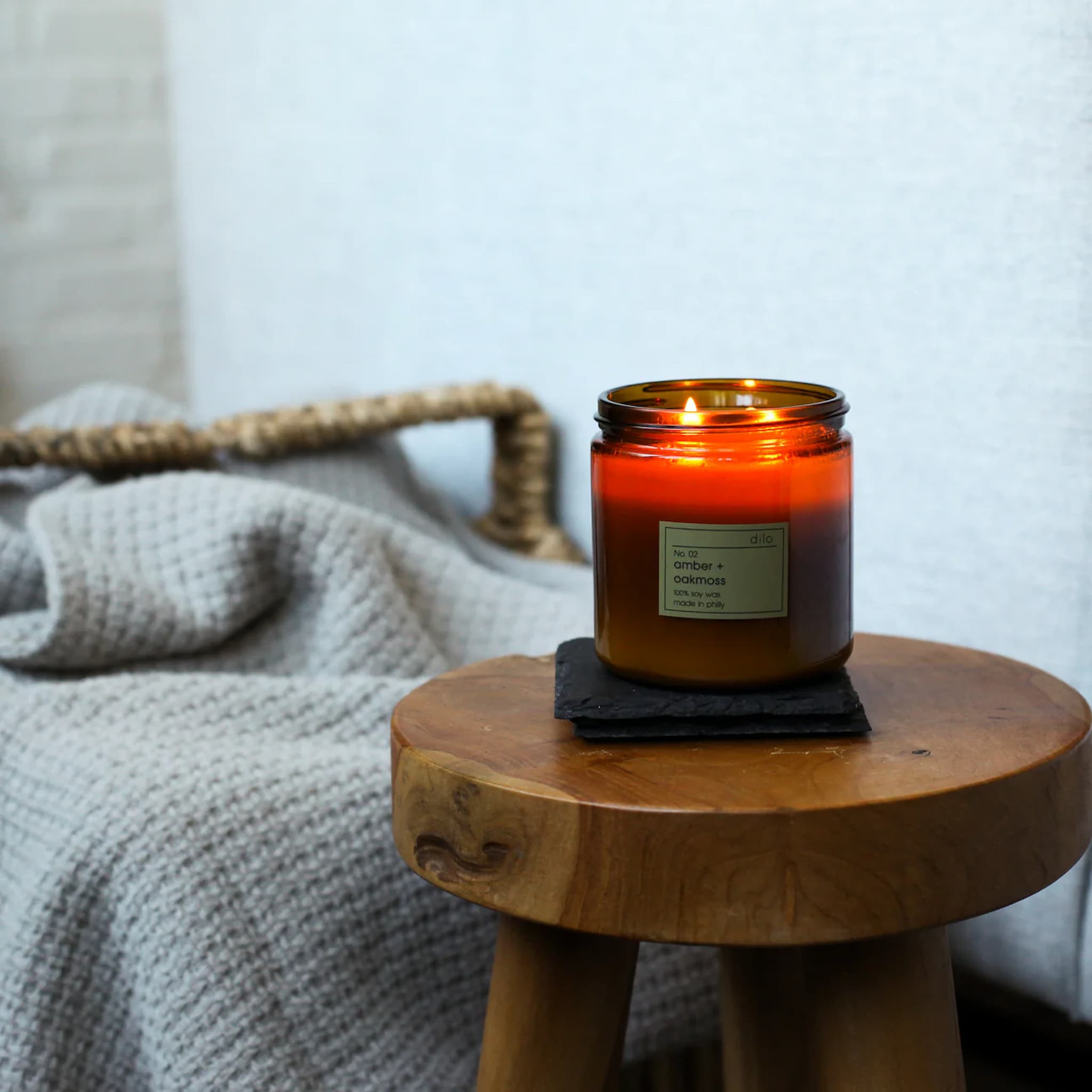Candle in an amber glass jar on a wooden stool with a soft blurred background