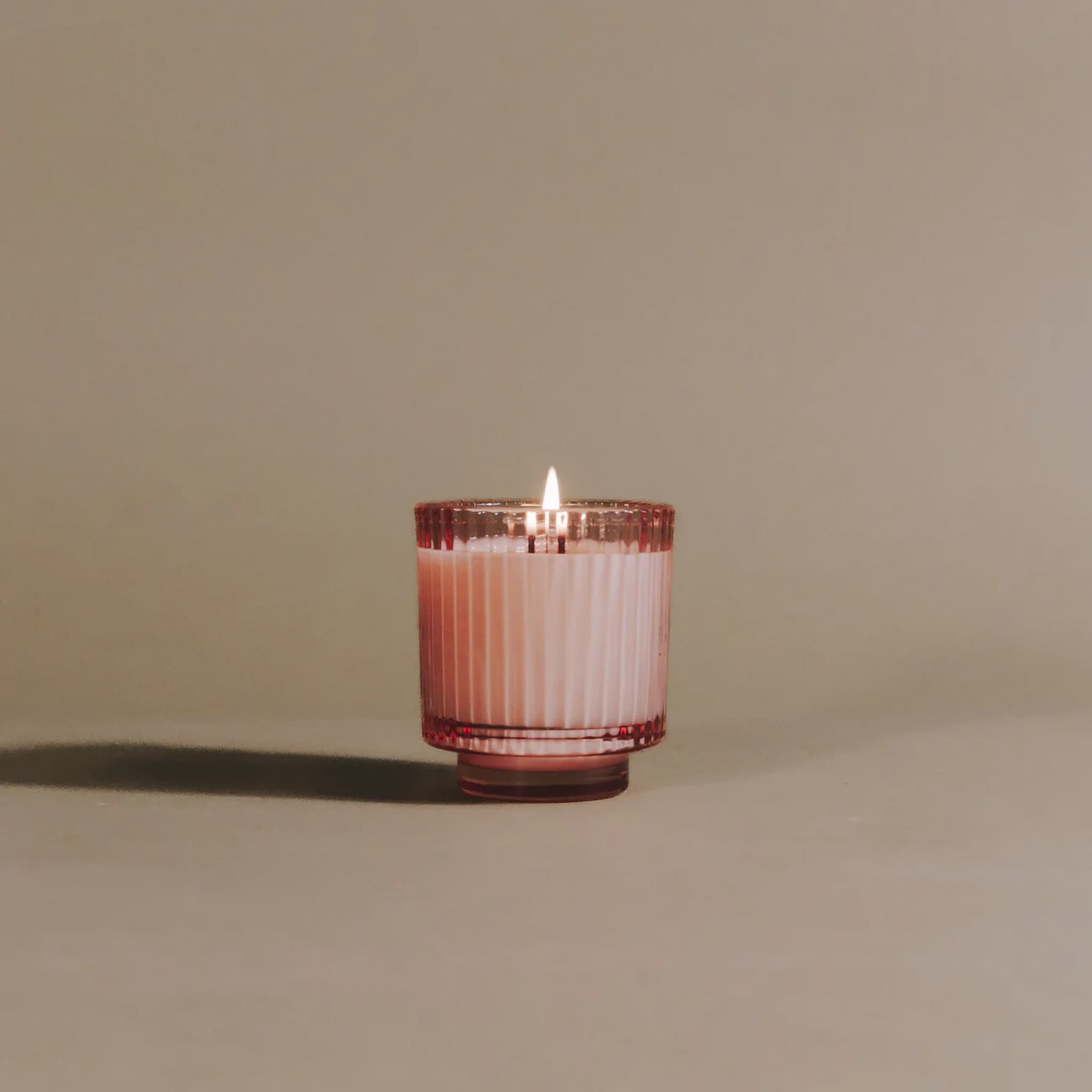 Candle in a pink ribbed glass container on a beige background