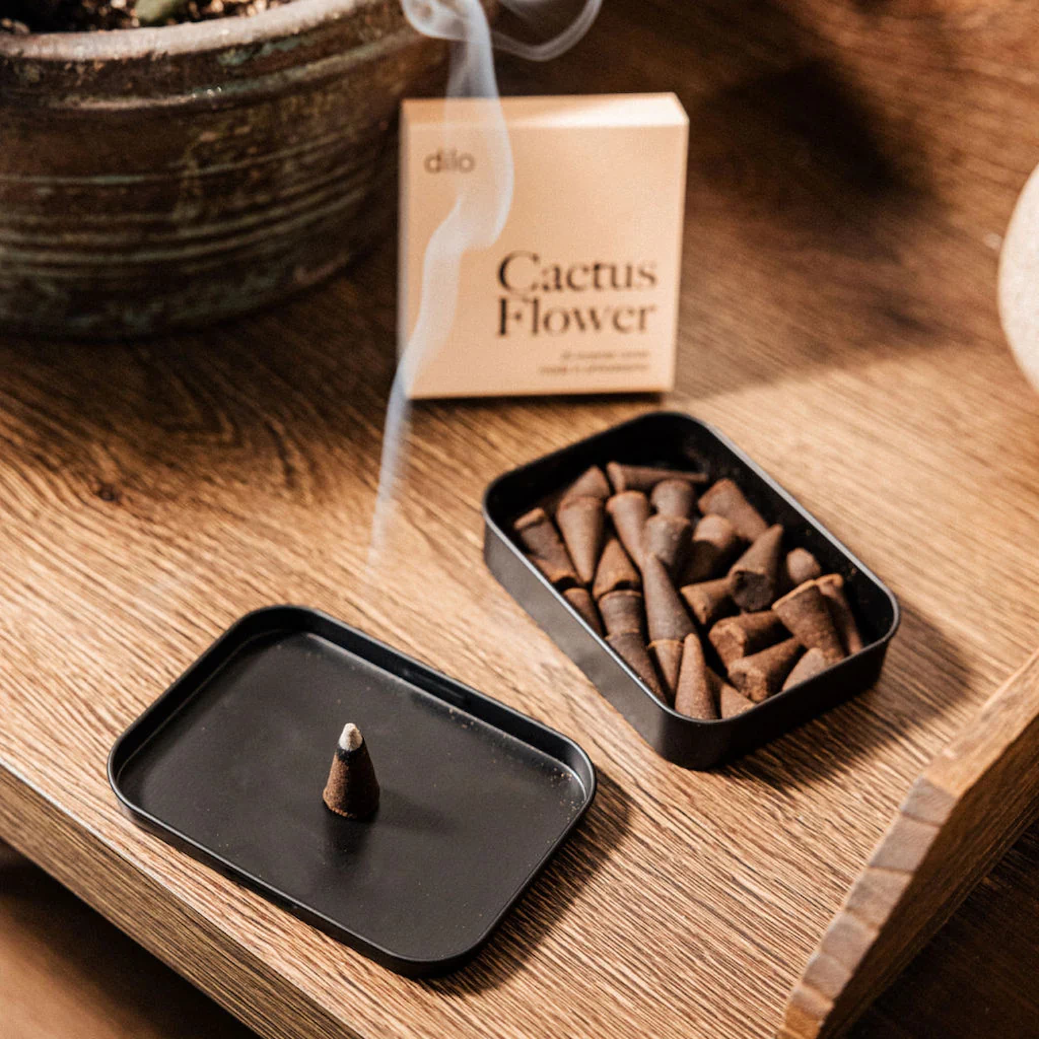 Incense cones in a box labeled 'Cactus Flower' on a wooden surface with an incense cone on a black tray.