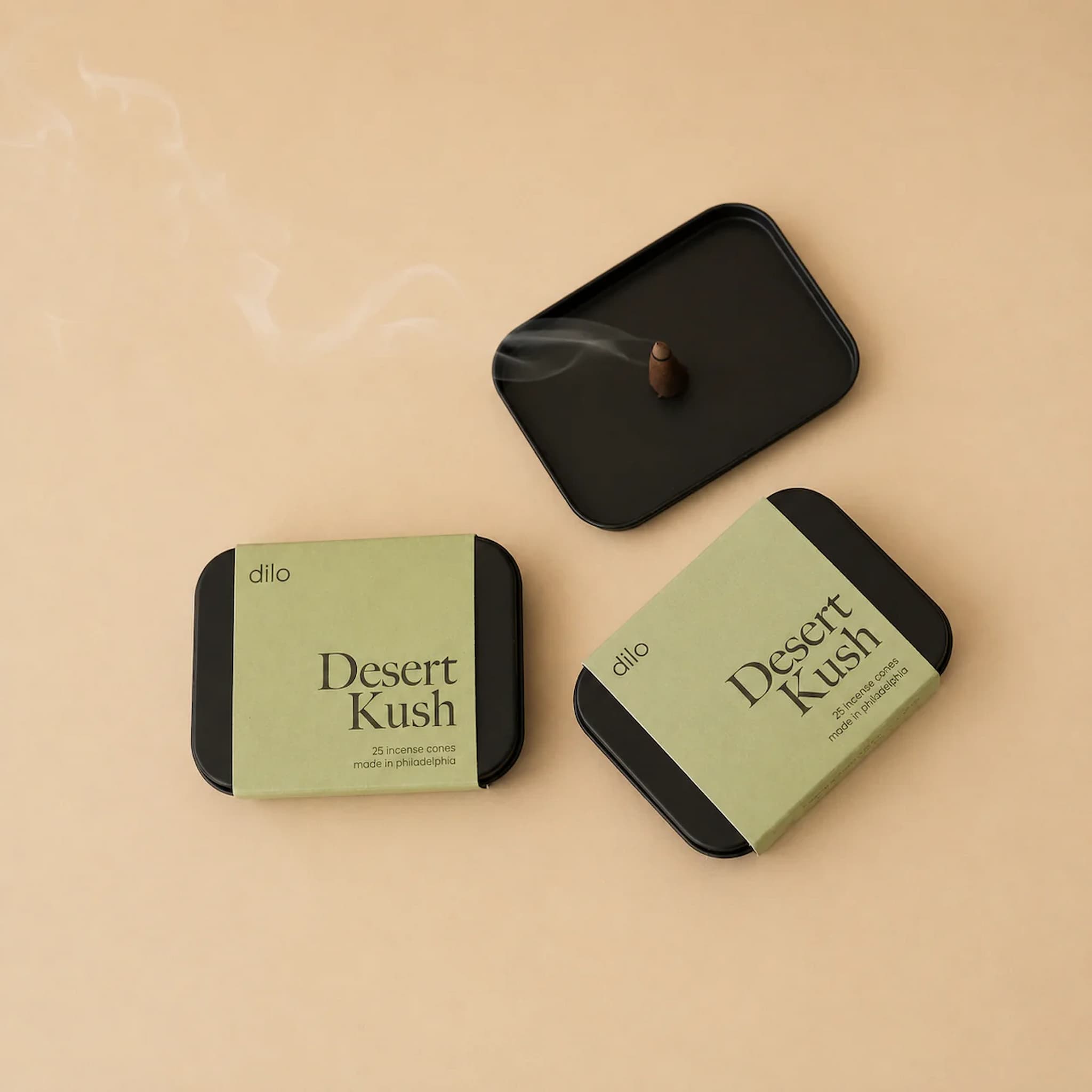 Two green containers labeled dilo 'Desert Kush' with a black lid holding an incense cone on a beige background.