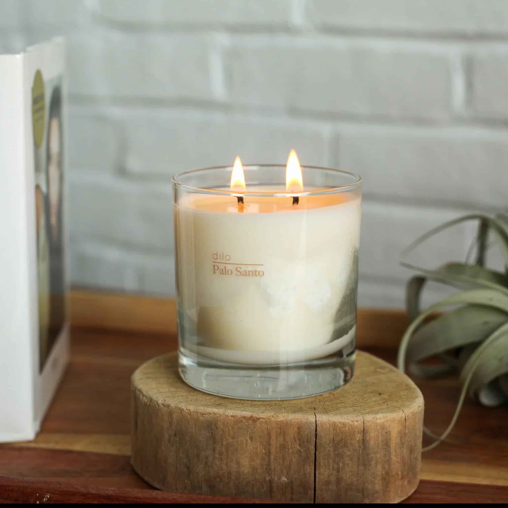 Dilo candle in a glass jar labeled 'Palo Santo' on a wooden surface with a blurred background