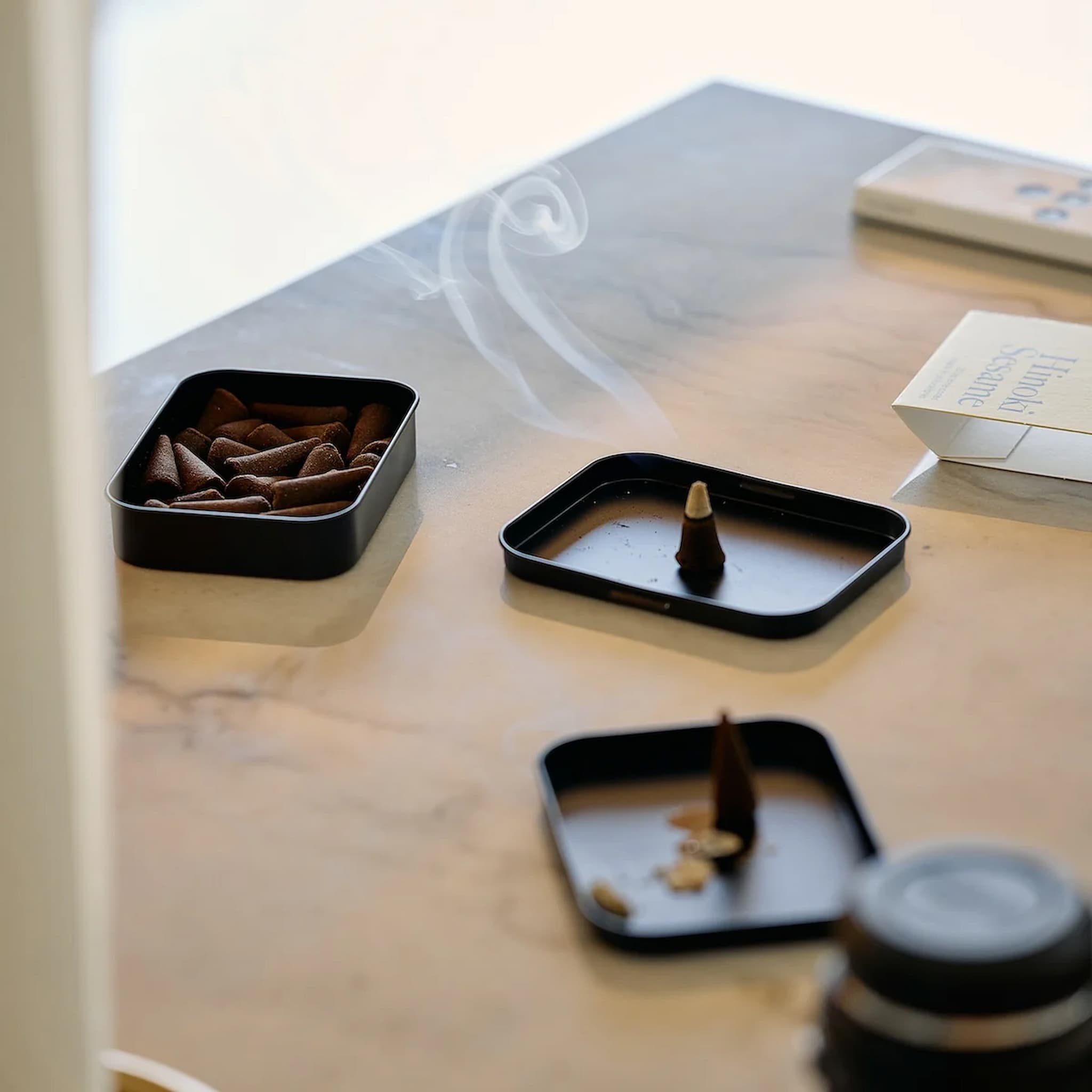 Incense cones in black containers on an off-white surface with a blurred background