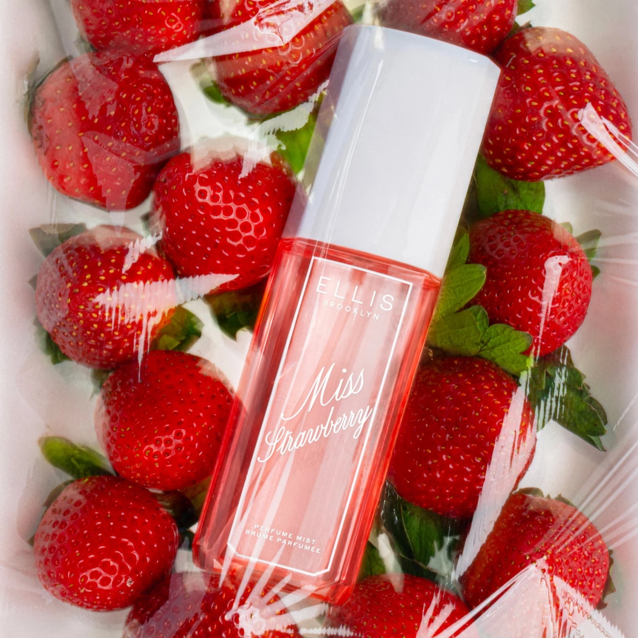 Ellis Brooklyn Miss Strawberry Perfume Mist bottle on tray of strawberries covered with cling film.
