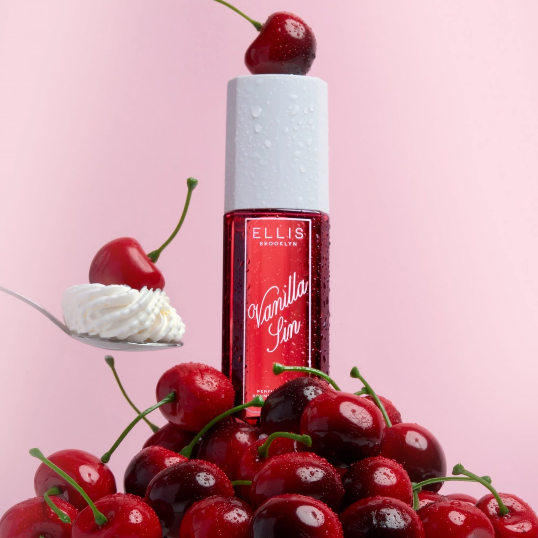 A bottle of Ellis Brooklyn Vanilla Sin Perfume Mist on a pile of cherries, with a cherry on top, and a spoon of whipped cream topped with a cherry to the left.
