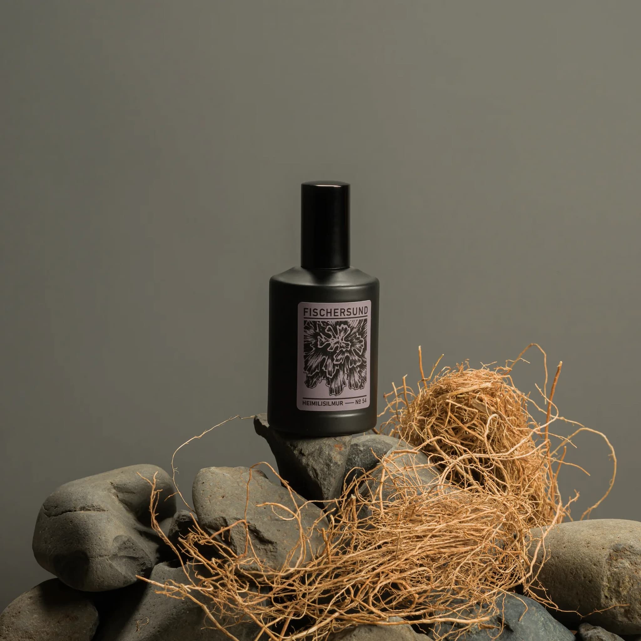 Bottle of Fischersund 54 room spray on a stone surface with hay, against a gray background