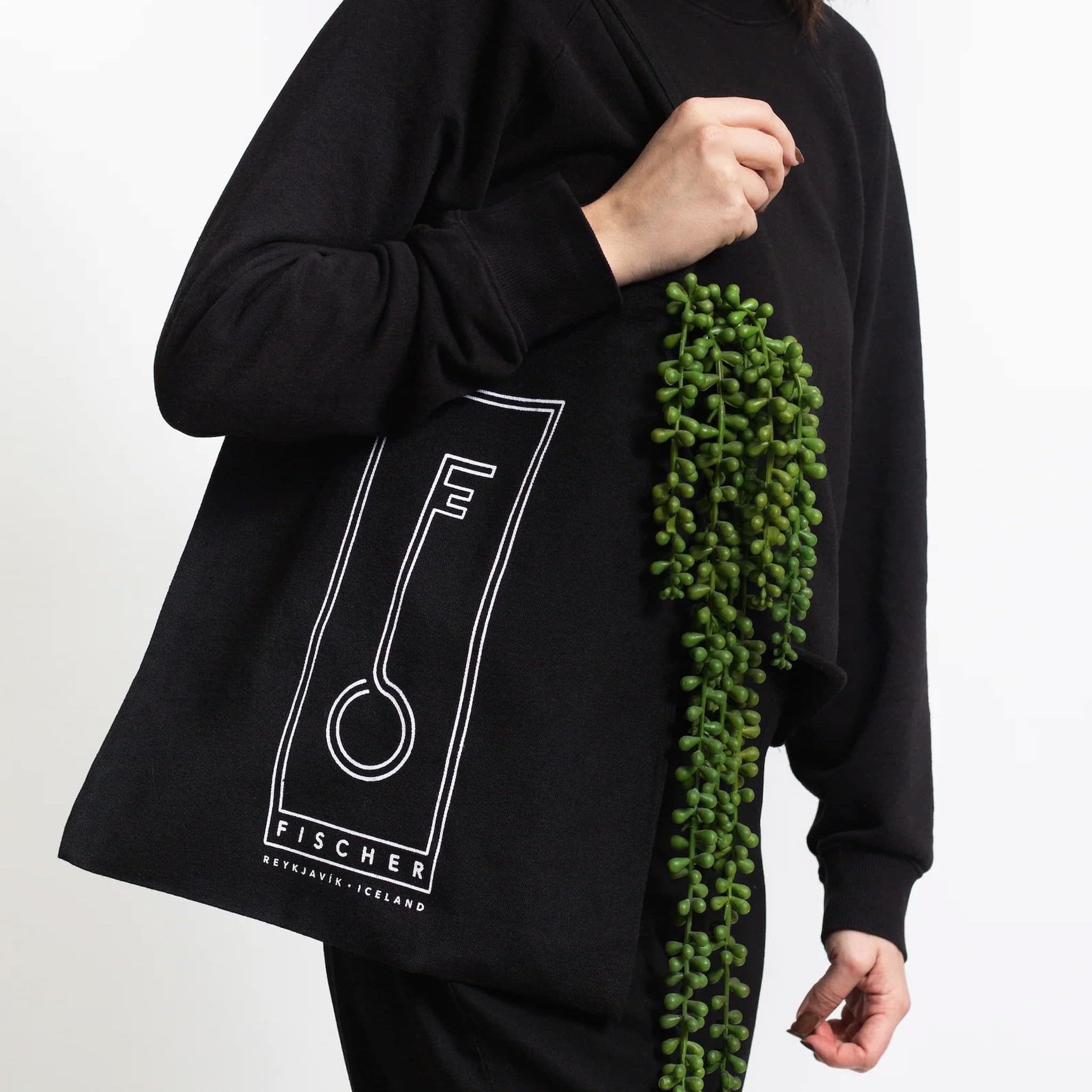 Person holding a black Fischersund tote bag with a white logo and text on a white background