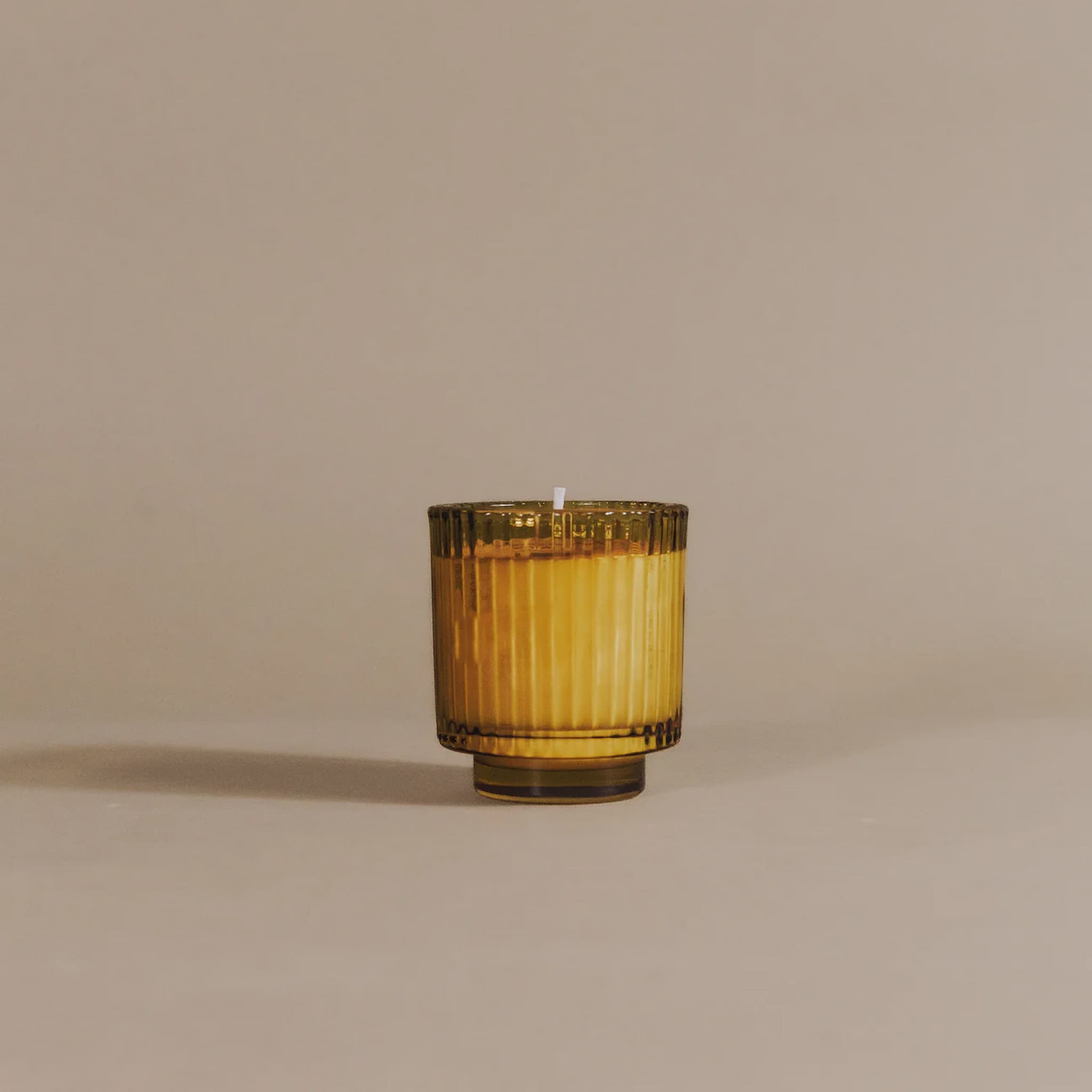 Golden yellow glass candle in a ribbed texture on a beige background