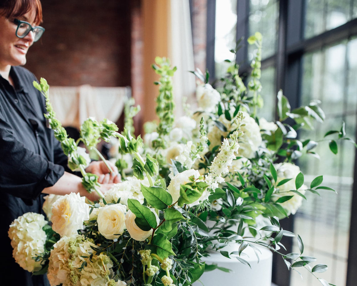 Hudson Valley wedding florist Jill Hilbrenner of Witch Hazel adjusts a large floral arrangement with white and green flowers at the Roundhouse in Beacon, NY.