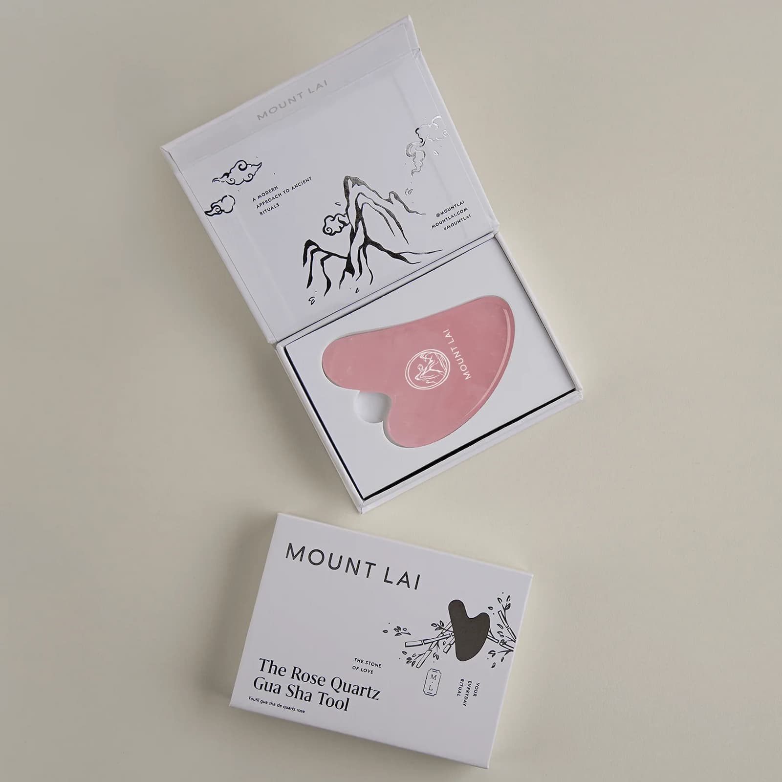 Pink Mount Lai Rose Quartz Gua Sha tool inside its white rectangular packaging, against a beige-grey background