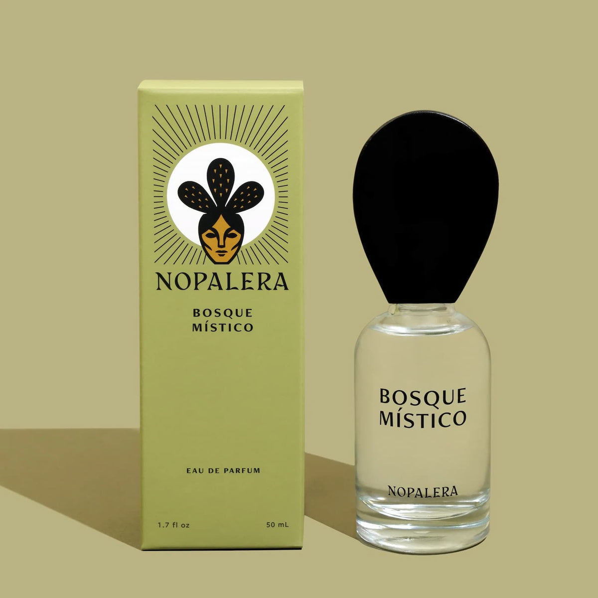 A glass bottle of Nopalera "Basque Mistico" perfume next to its green packaging box against a lighter green background.