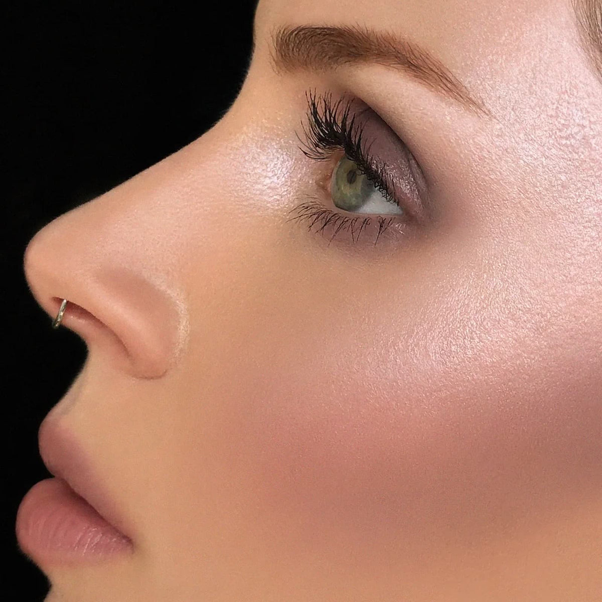 A close-up of a model's face against a black background. They are wearing Rituel de Fille Inner Glow Creme Pigment in "Intuition".