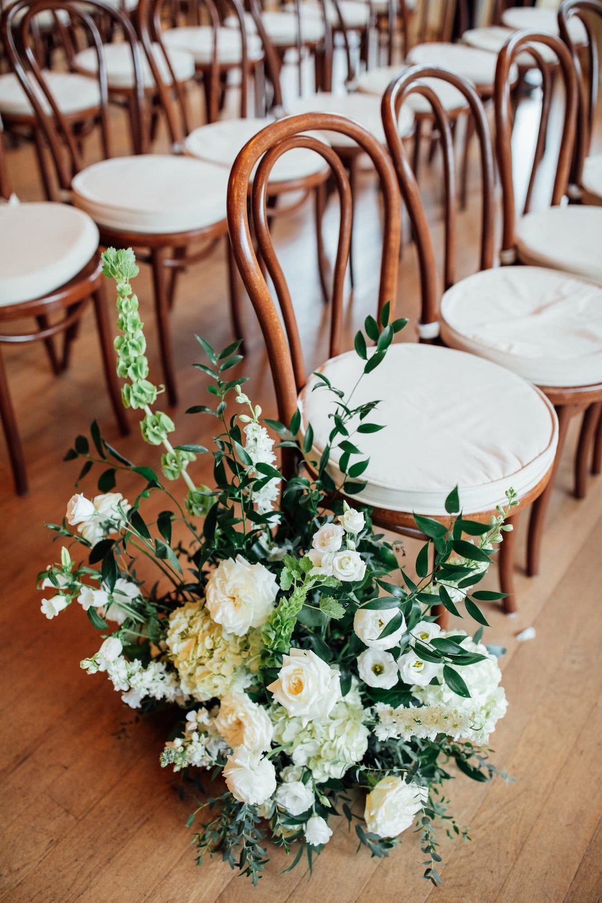 A Roundhouse wedding aisle flower arrangement by Witch Hazel with white and pale green flowers and green foliage.