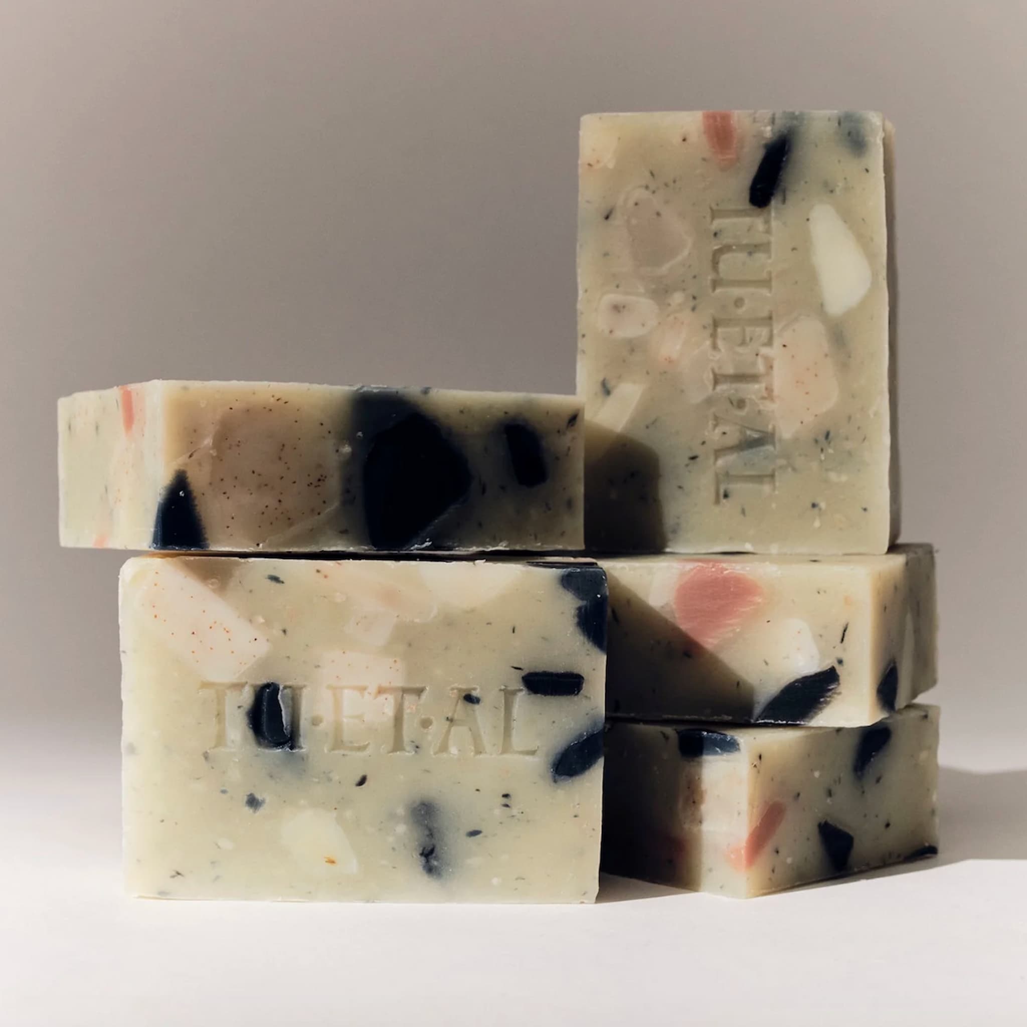 Stack of speckled soap bars with 'TU ET AL' branding on a neutral background