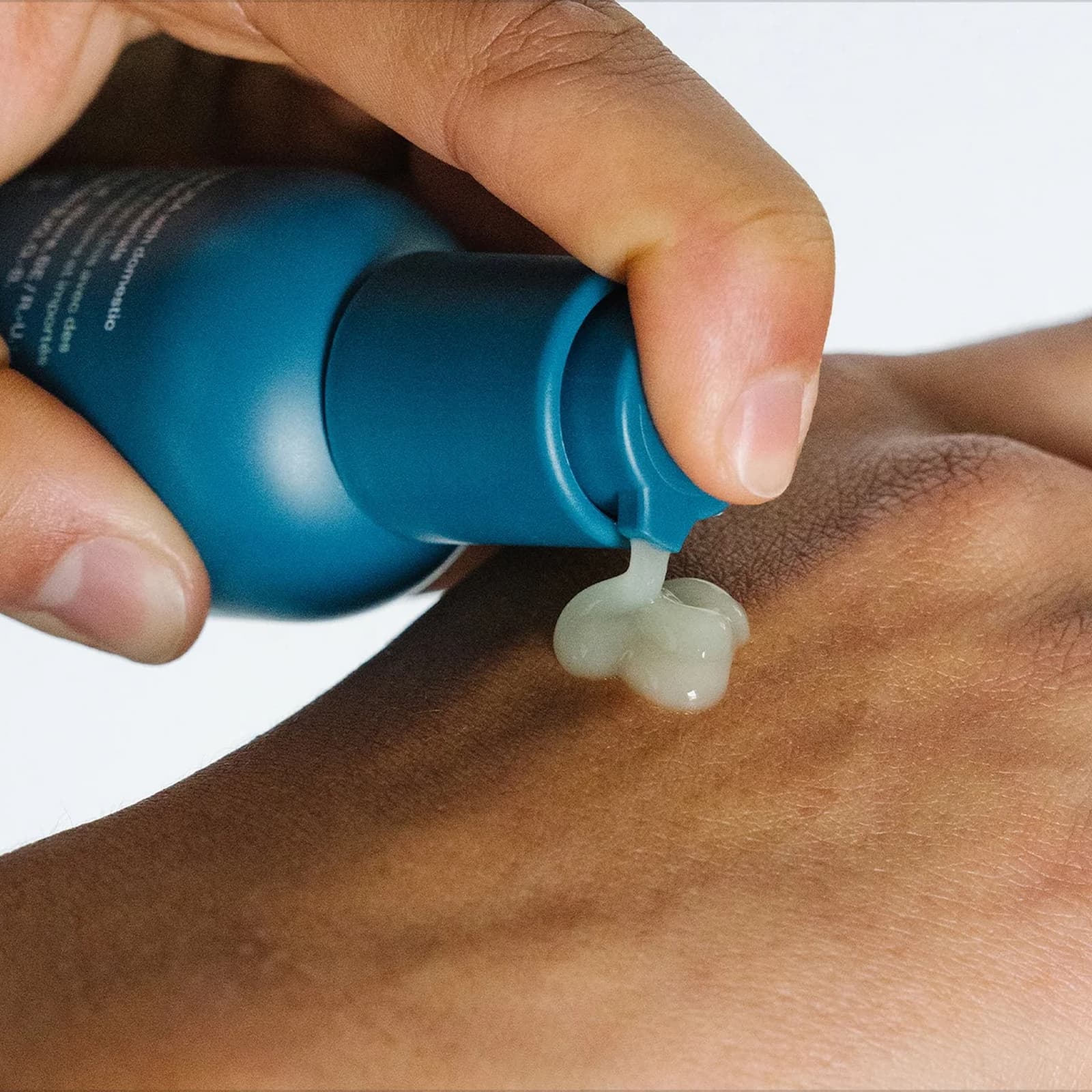 A hand is applying a light green pump of Ursa Major Forest Water Hyaluronic Serum from a blue bottle onto their other hand.
