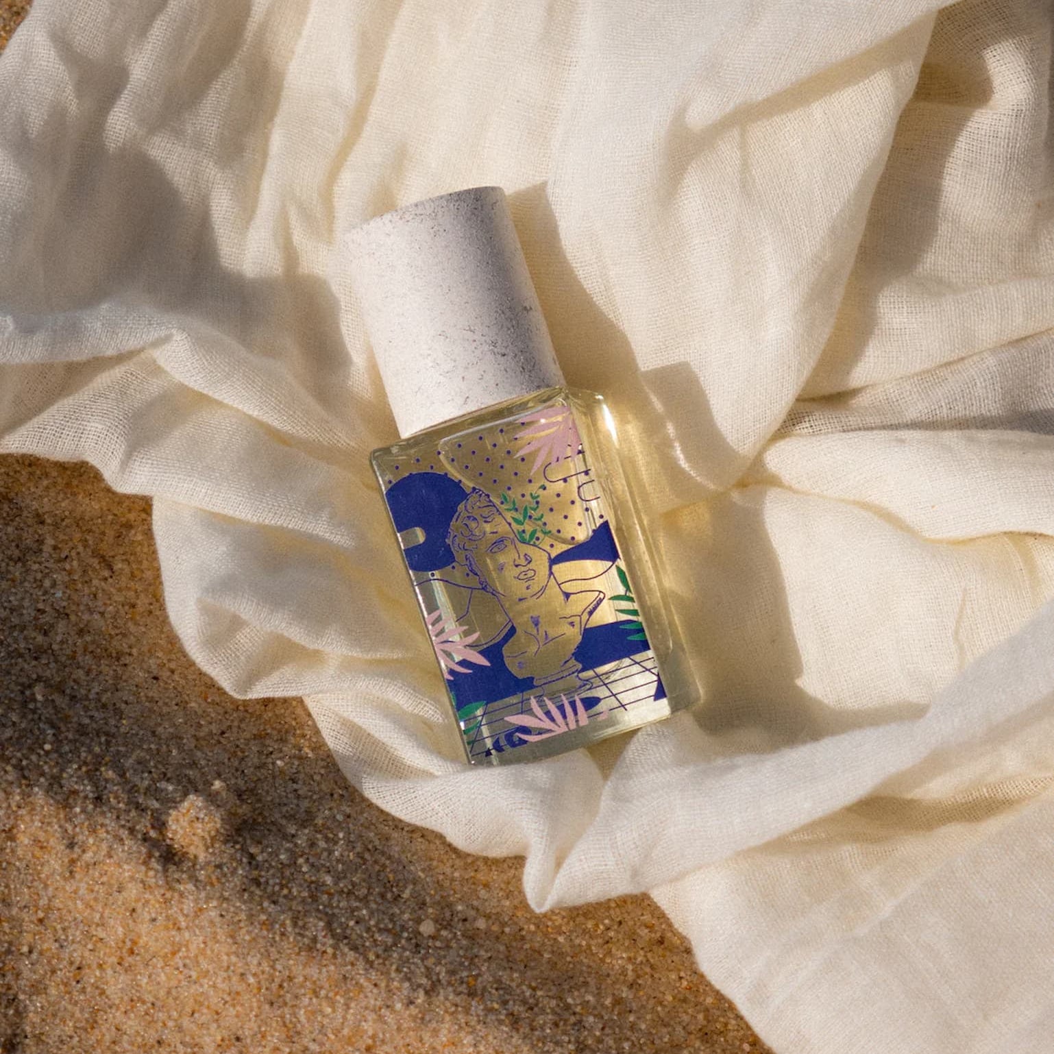 Small bottle with a colorful label on a white fabric background on sand.