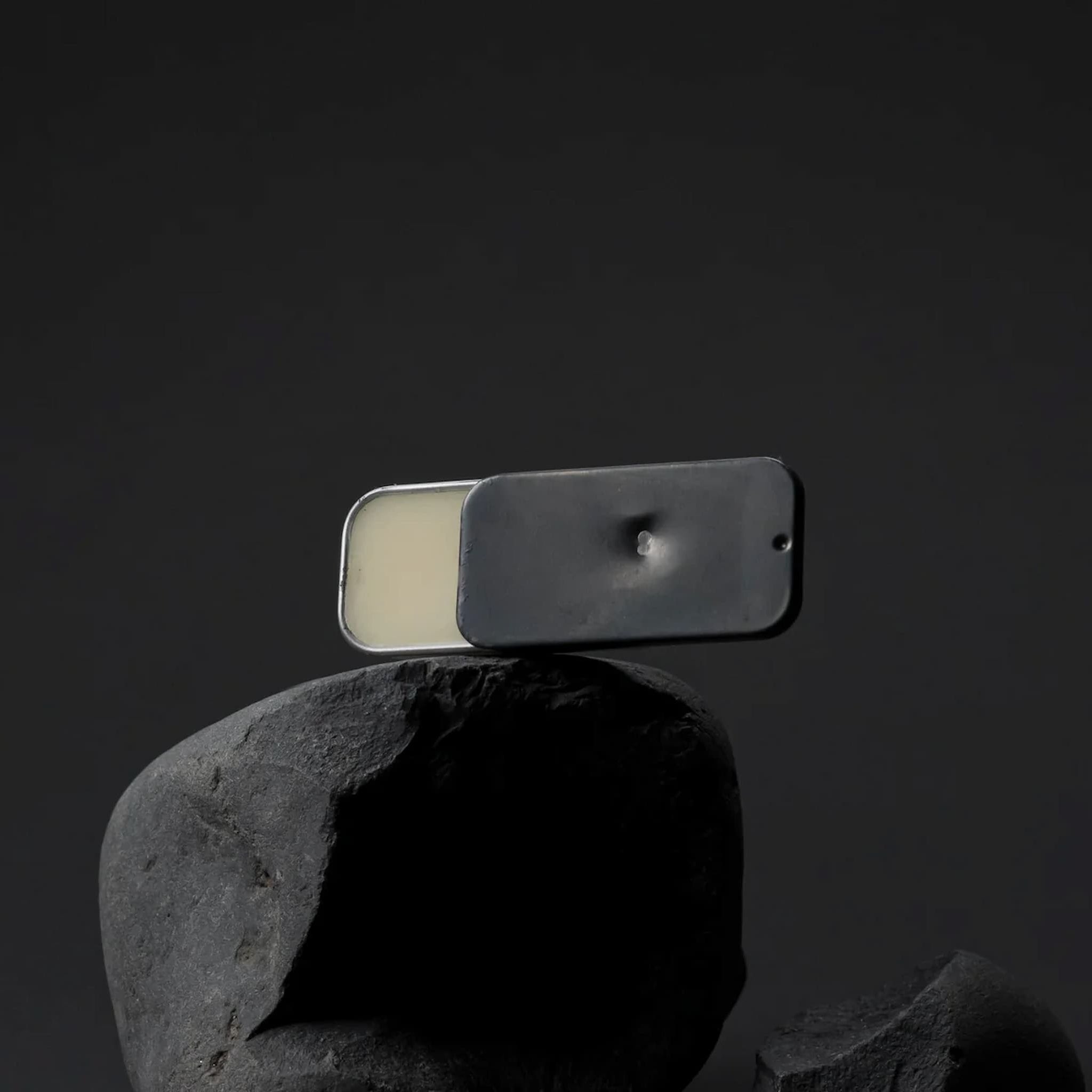 Tin of Fischersund solid perfume  balanced on a large stone against a dark background