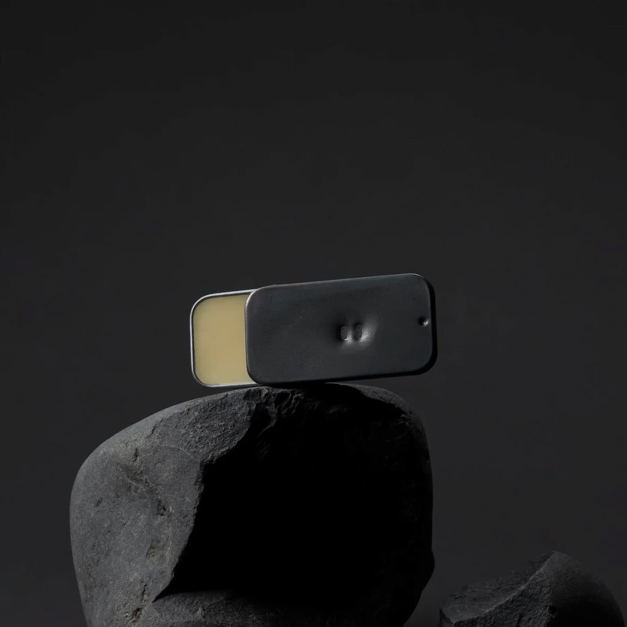 Metallic tin holding Fischersund solid perfume balanced on a rock against a gray background