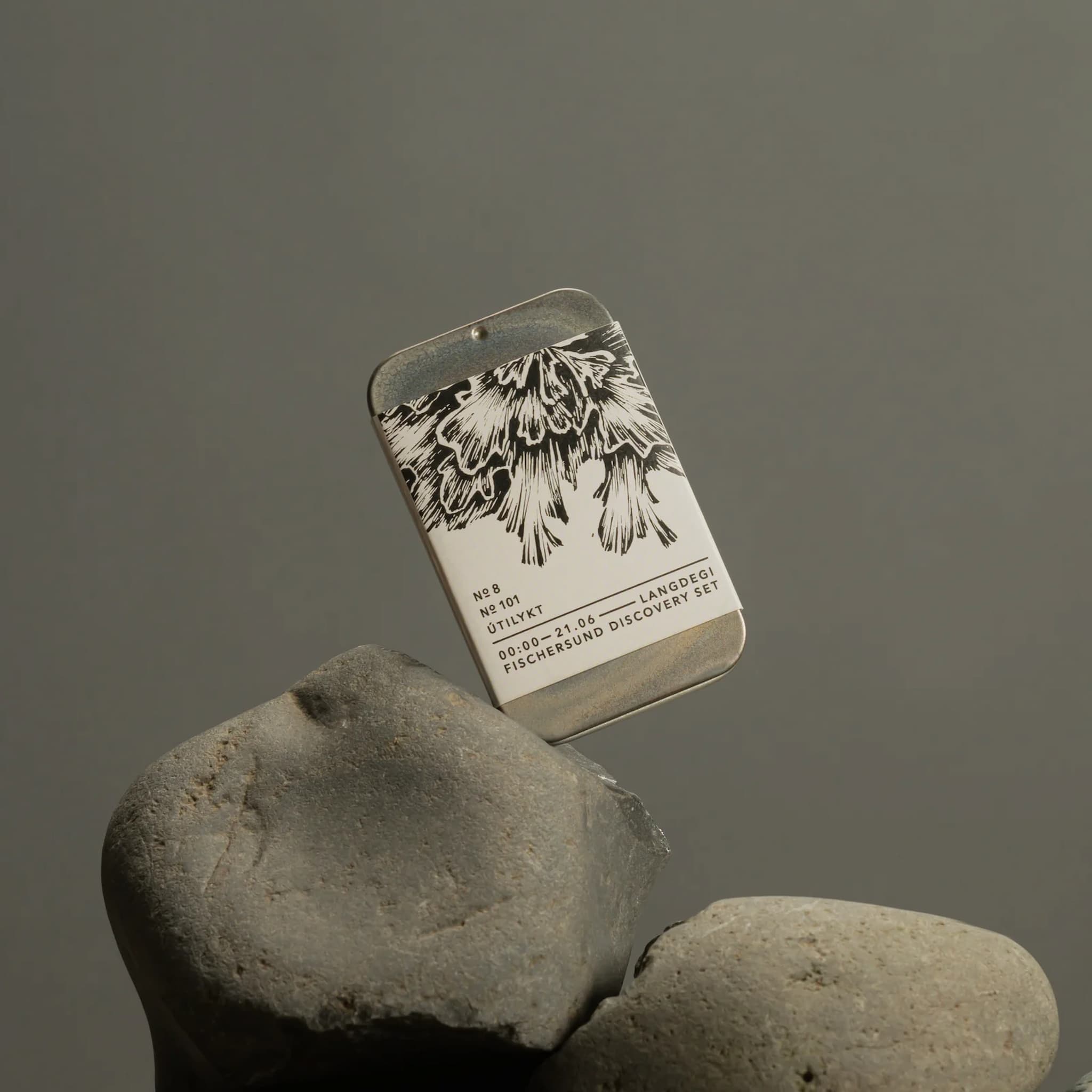 Fischersund Langdegi Light Discovery Set tin with engraved design on a rock against a gray background