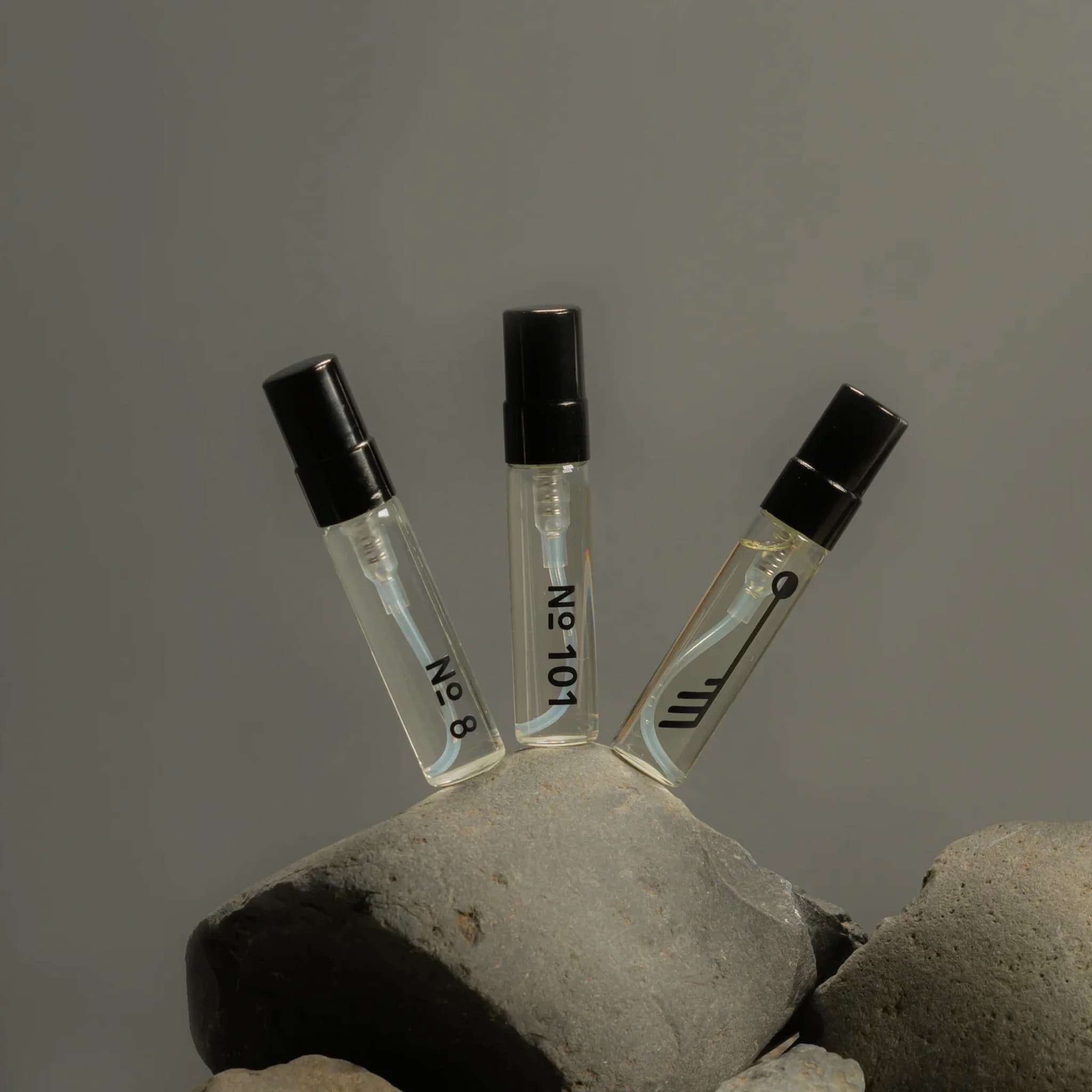 Three Fischersund perfume vials with black caps on a stone surface against a gray background