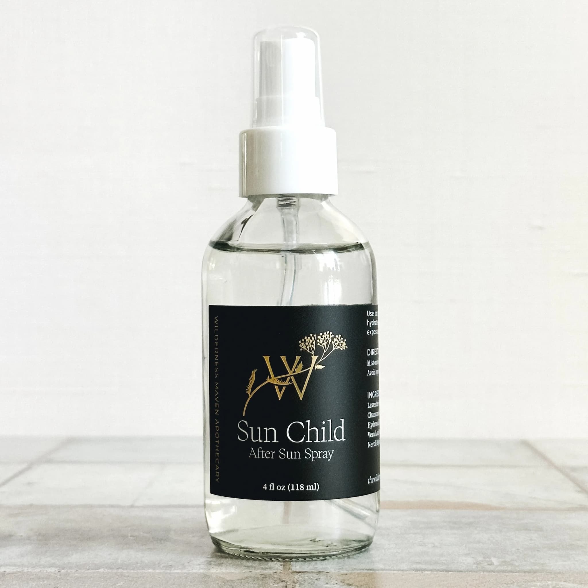 Clear spray bottle labeled 'Sun Child After Sun Spray' on a light wooden surface with a white background