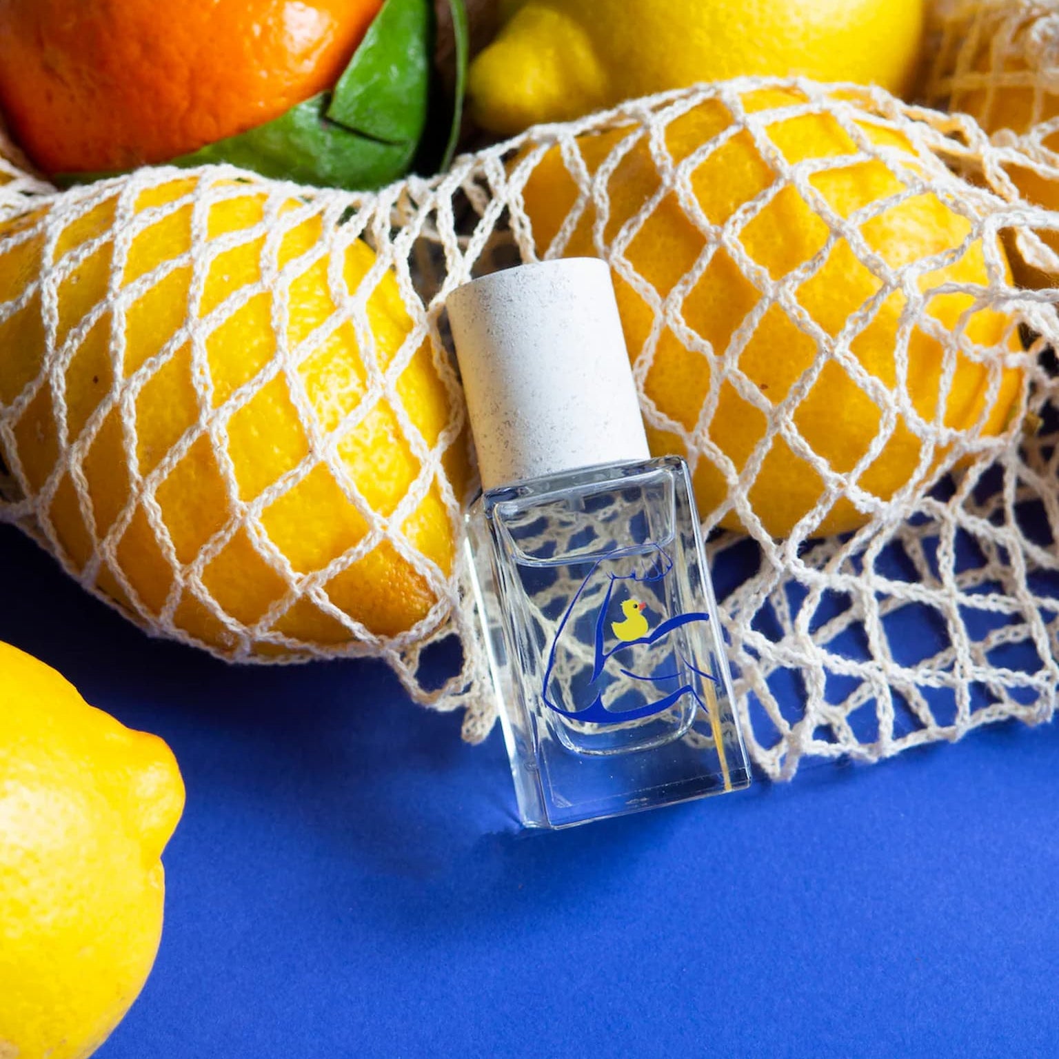 Small bottle of perfume on a blue background with lemons and an orange.