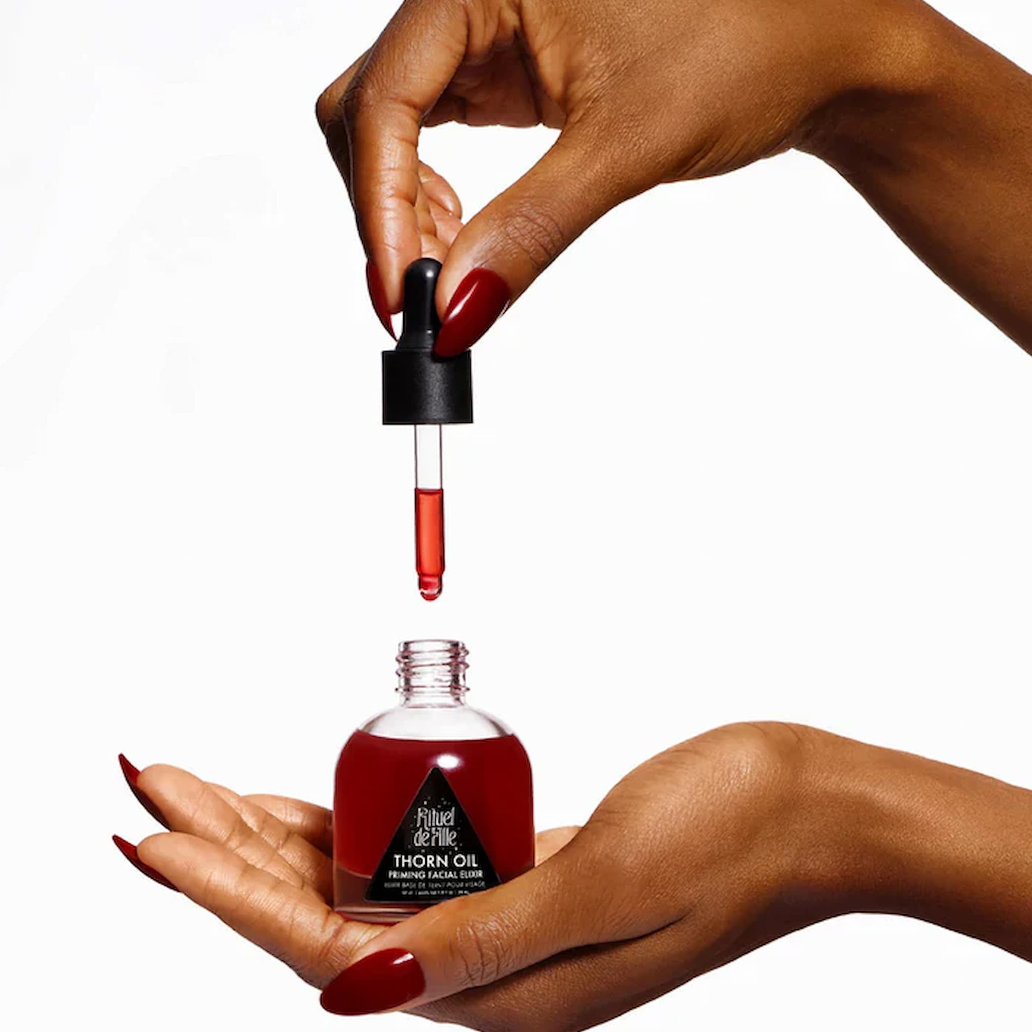 Hand holding a dropper with red liquid over a bottle labeled 'Thorn Oil' on a white background