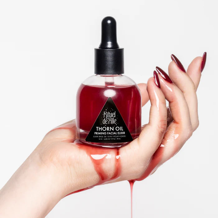 Hand holding a bottle of Rituel de Fille Thorn Oil with red liquid on a white background