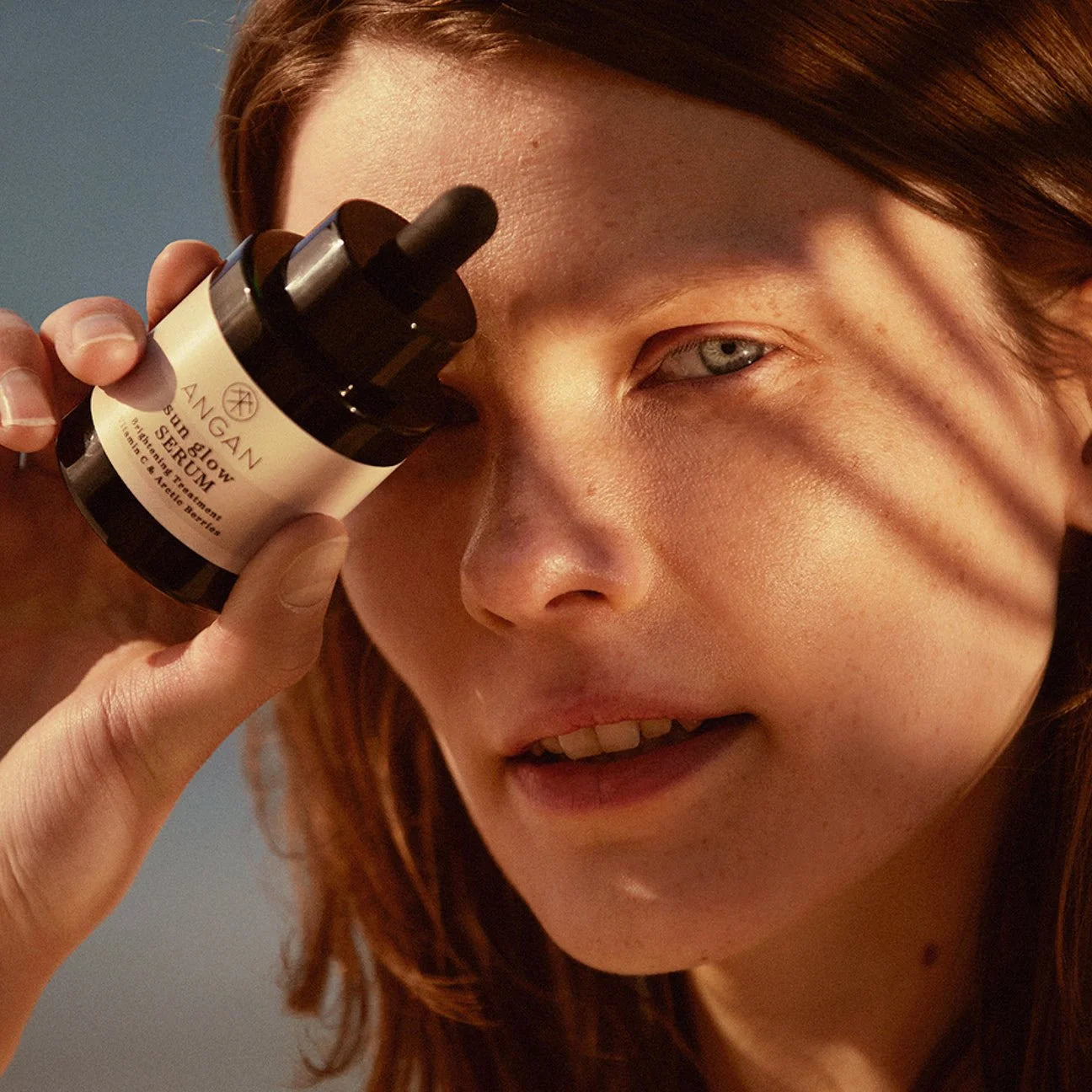 Person holding a bottle of Angan skincare serum close to their face against a blurred natural background