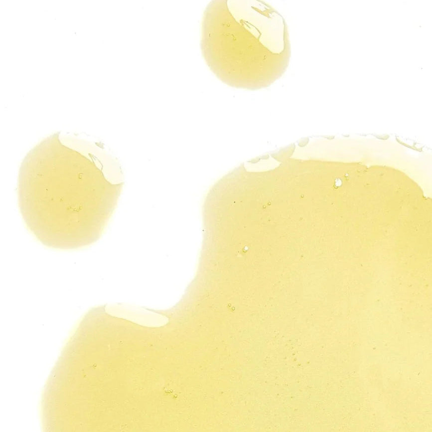 Close-up of yellow oil cleanser with droplets on a white background