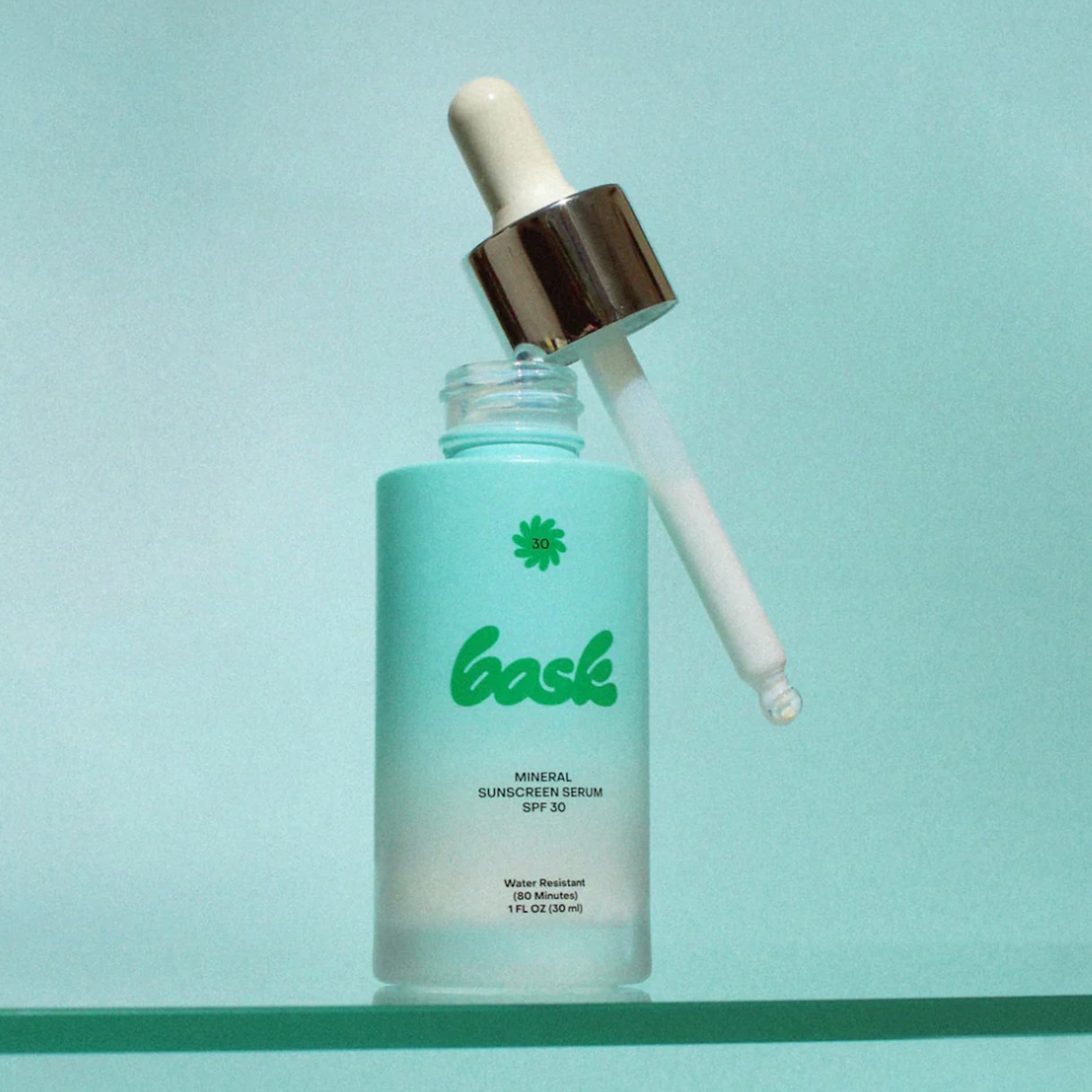 Bask SPF 30 Mineral Sunscreen Serum, open on a glass counter on a blue background. 