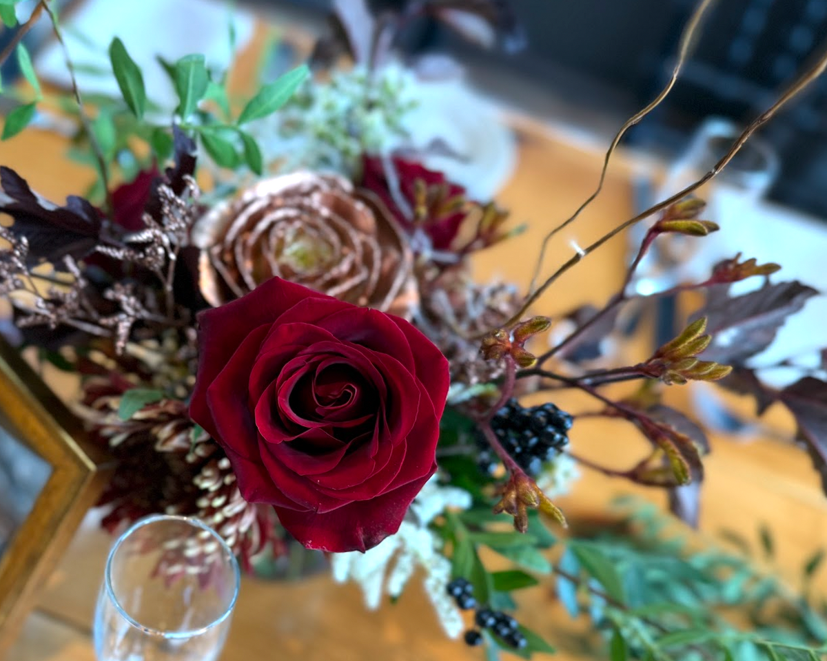 Diamond Mills wedding centerpiece in the Hudson Valley featuring a Black Magic rose, copper kale, pepper berries, and greenery.