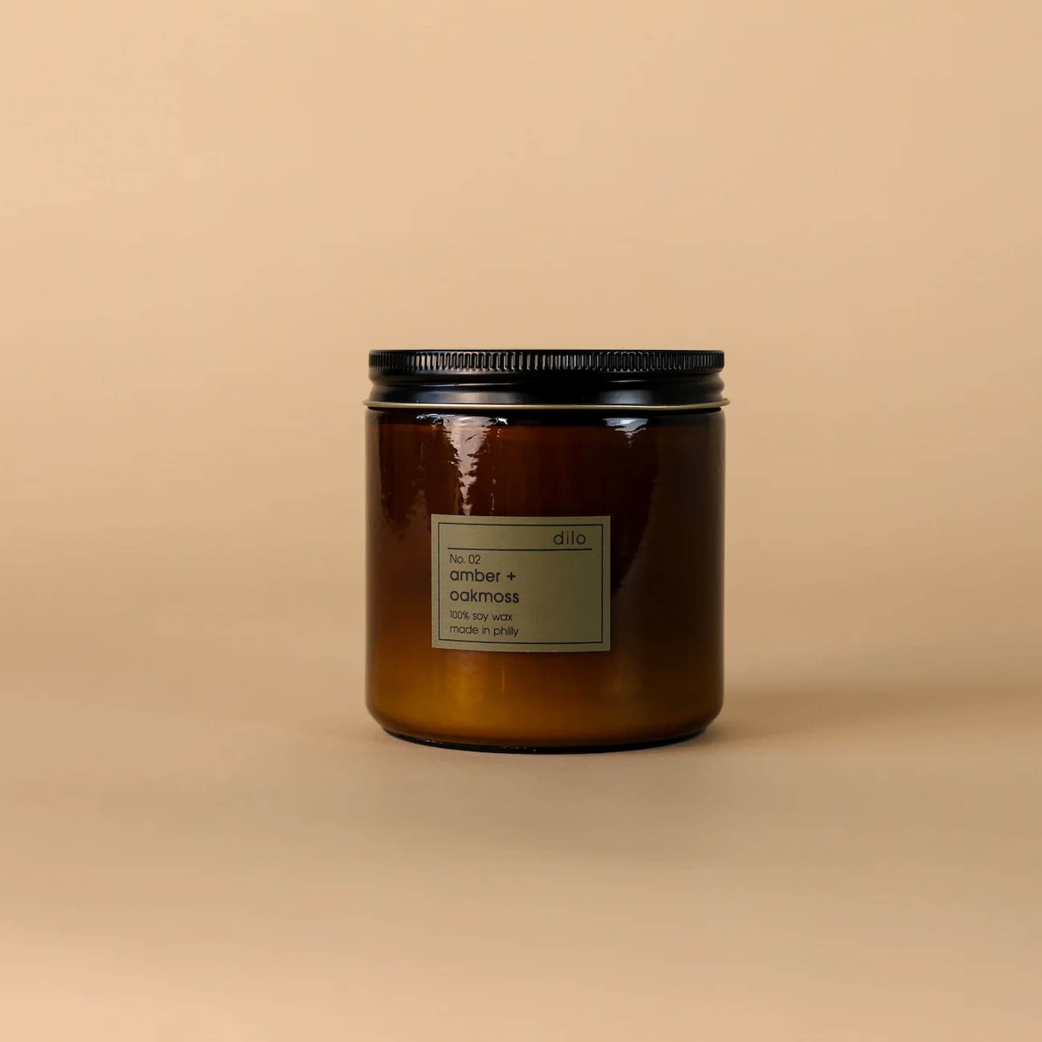 Amber glass candle jar with black lid on a beige background