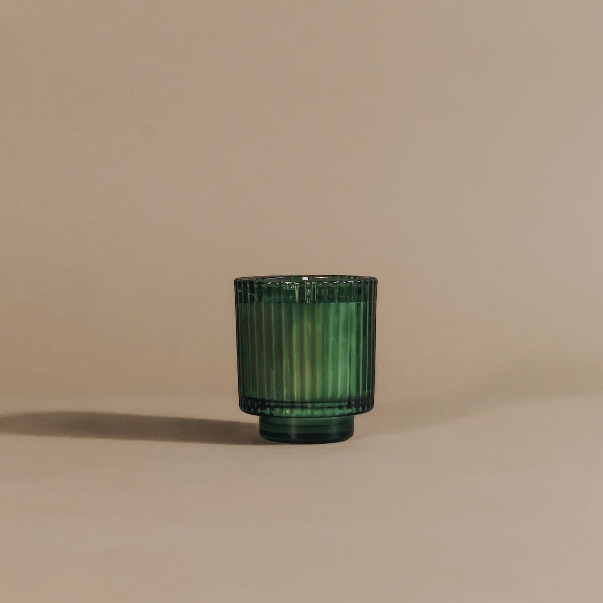Green glass candle holder on a beige background