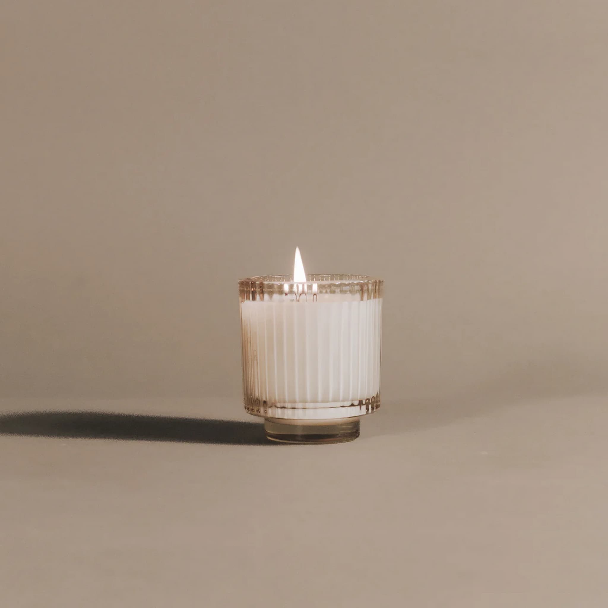 Candle in a glass container with a ribbed texture on a beige background