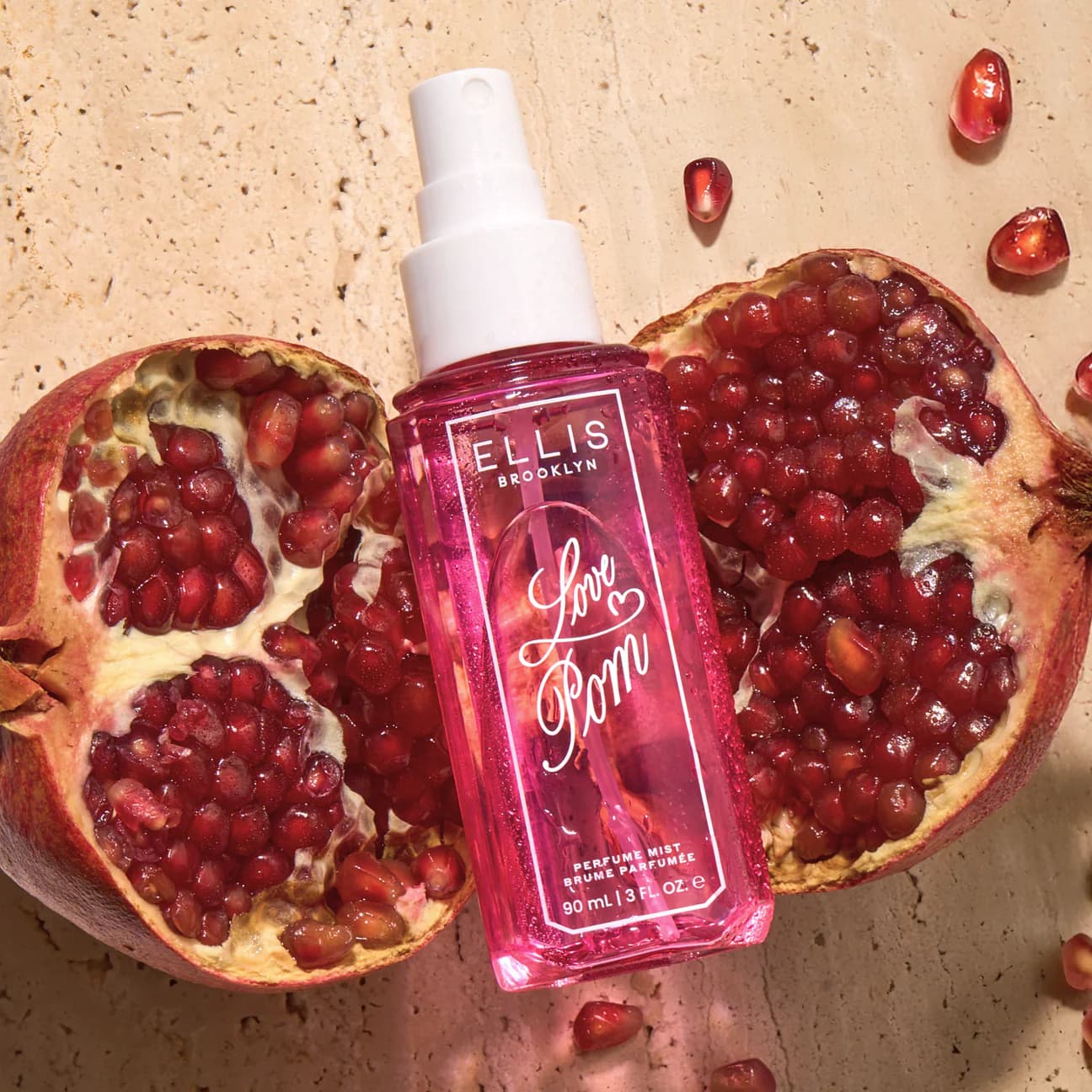 Perfume bottle with 'Ellis Brooklyn Love Pom' label surrounded by pomegranate fruits on a textured surface.