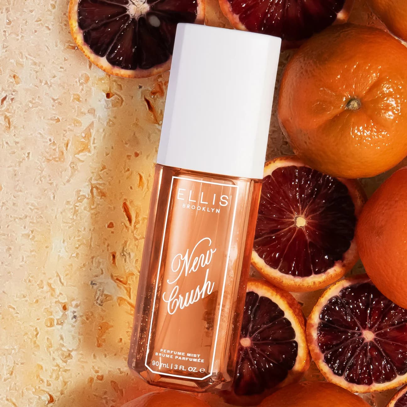 Ellis Brooklyn New Crush perfume mist bottle surrounded by sliced blood oranges on a textured surface.