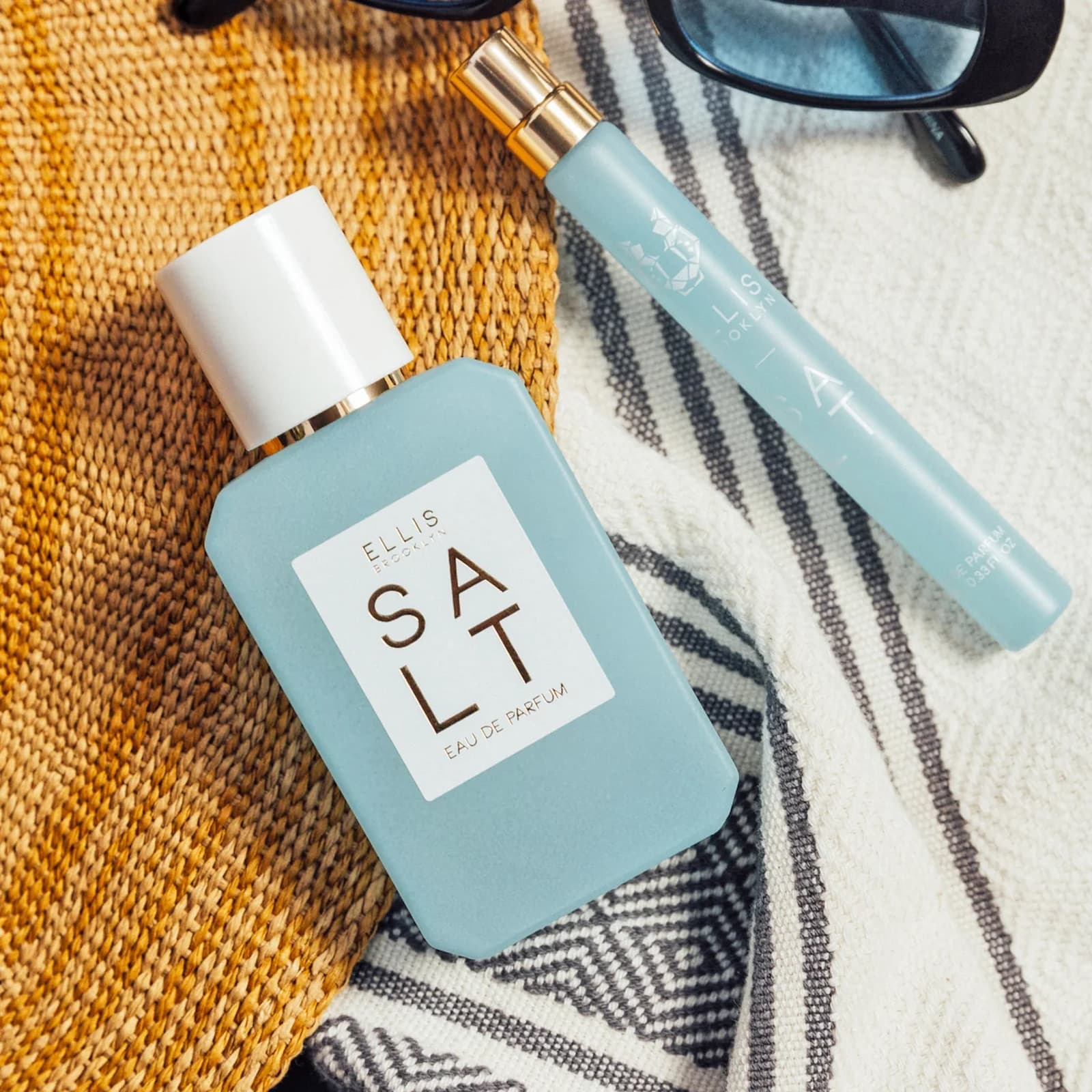 Two light blue bottles of Ellis Brooklyn Salt perfume sat against tan and white fabric.