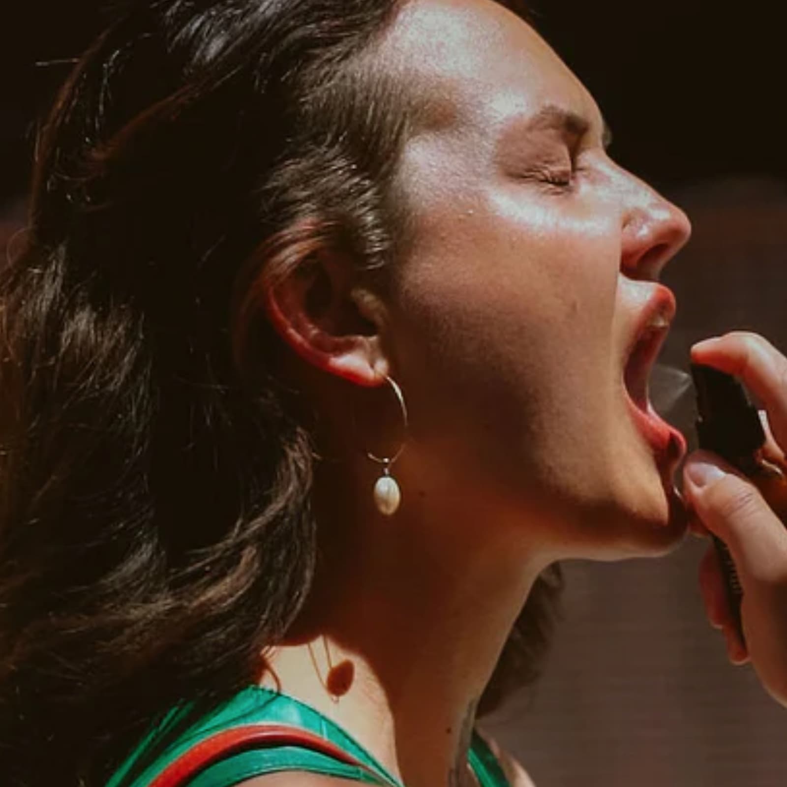 A woman with her mouth open is spraying Fat and the Moon Herbs the Word Mouth Spray into her mouth.