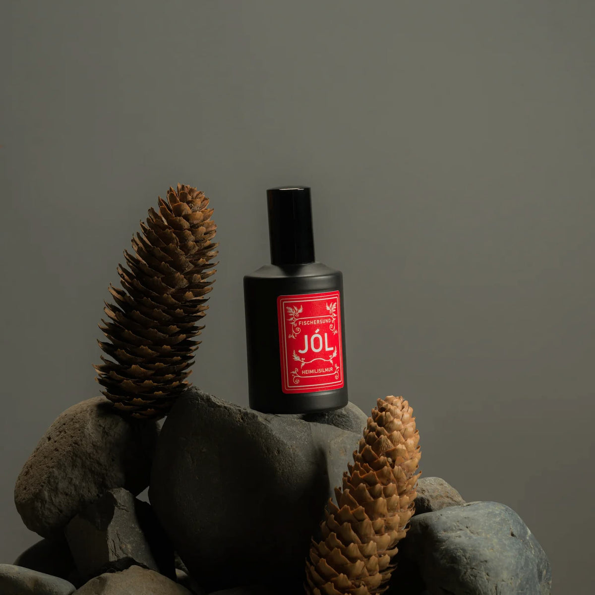 Fischersund Jol room spray bottle with red label on a rock with pine cones against a gray background